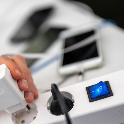 Ein Mann zieht den Stecker eines Ladegeräts für ein Smartphone aus einer Steckdosenleiste.