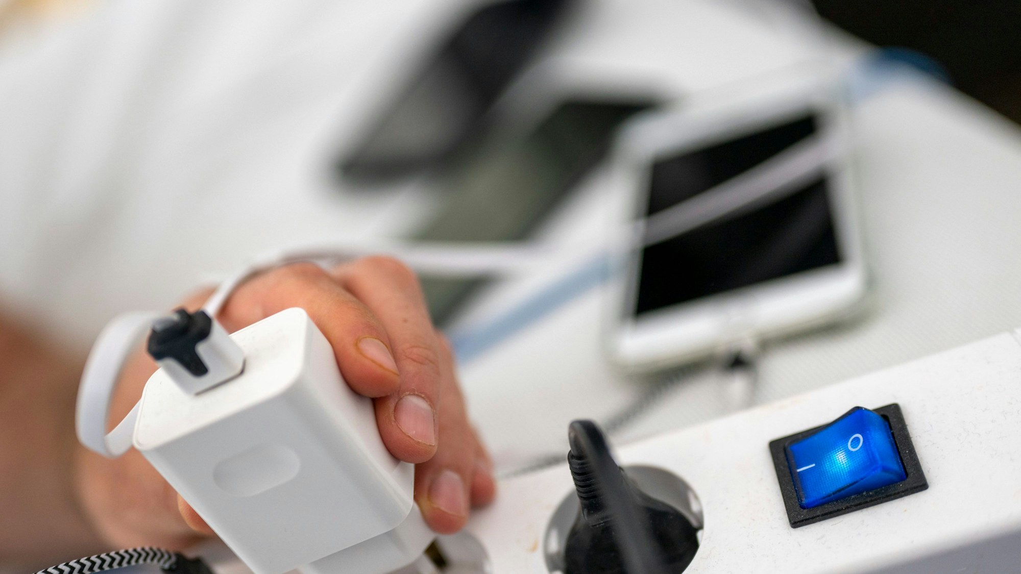 Ein Mann zieht den Stecker eines Ladegeräts für ein Smartphone aus einer Steckdosenleiste.