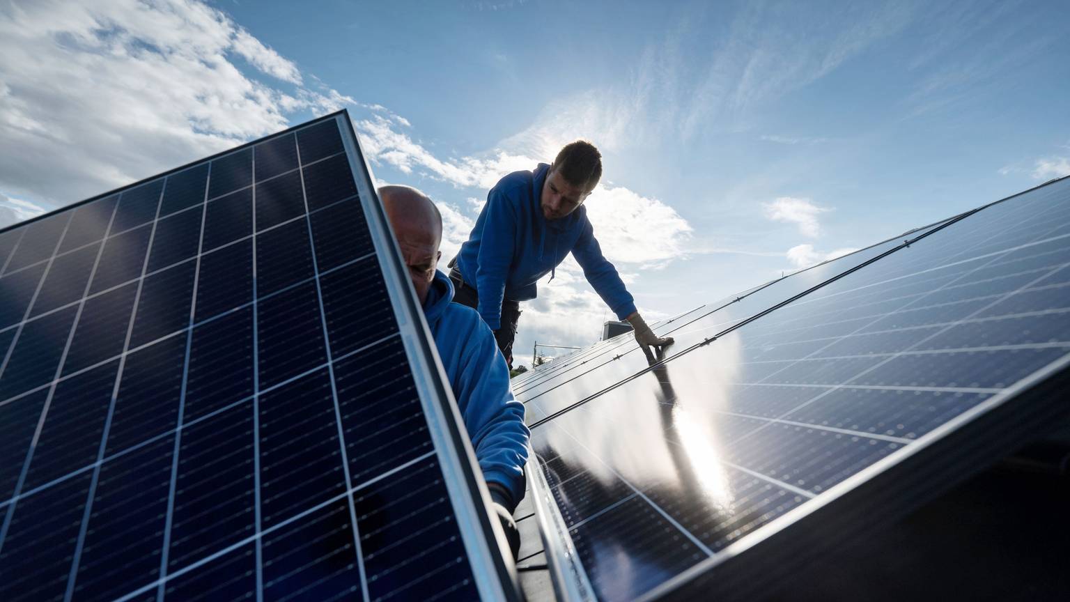 Arbeiter montieren Photovoltaikmodule auf dem Dach eines Wohnhauses.