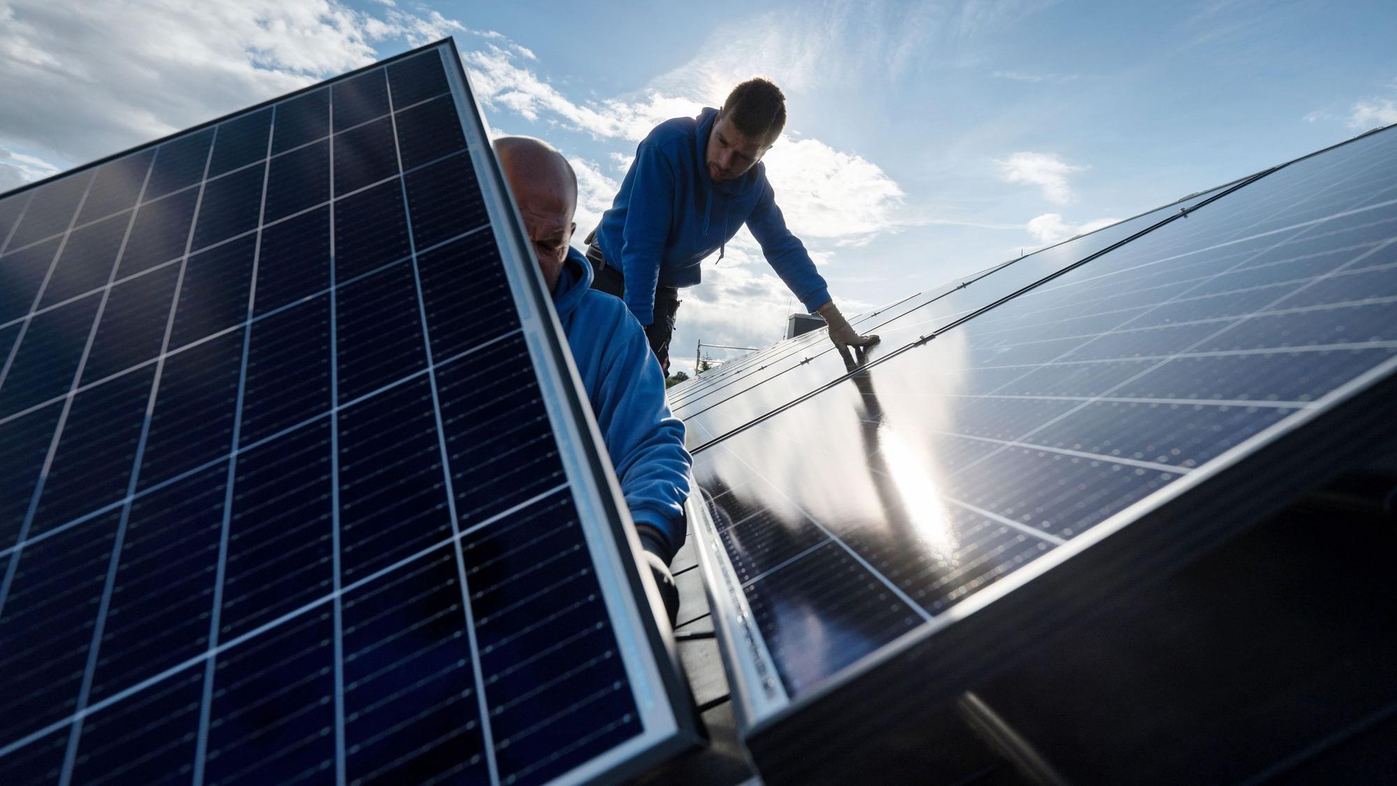 Arbeiter montieren Photovoltaikmodule auf dem Dach eines Wohnhauses.