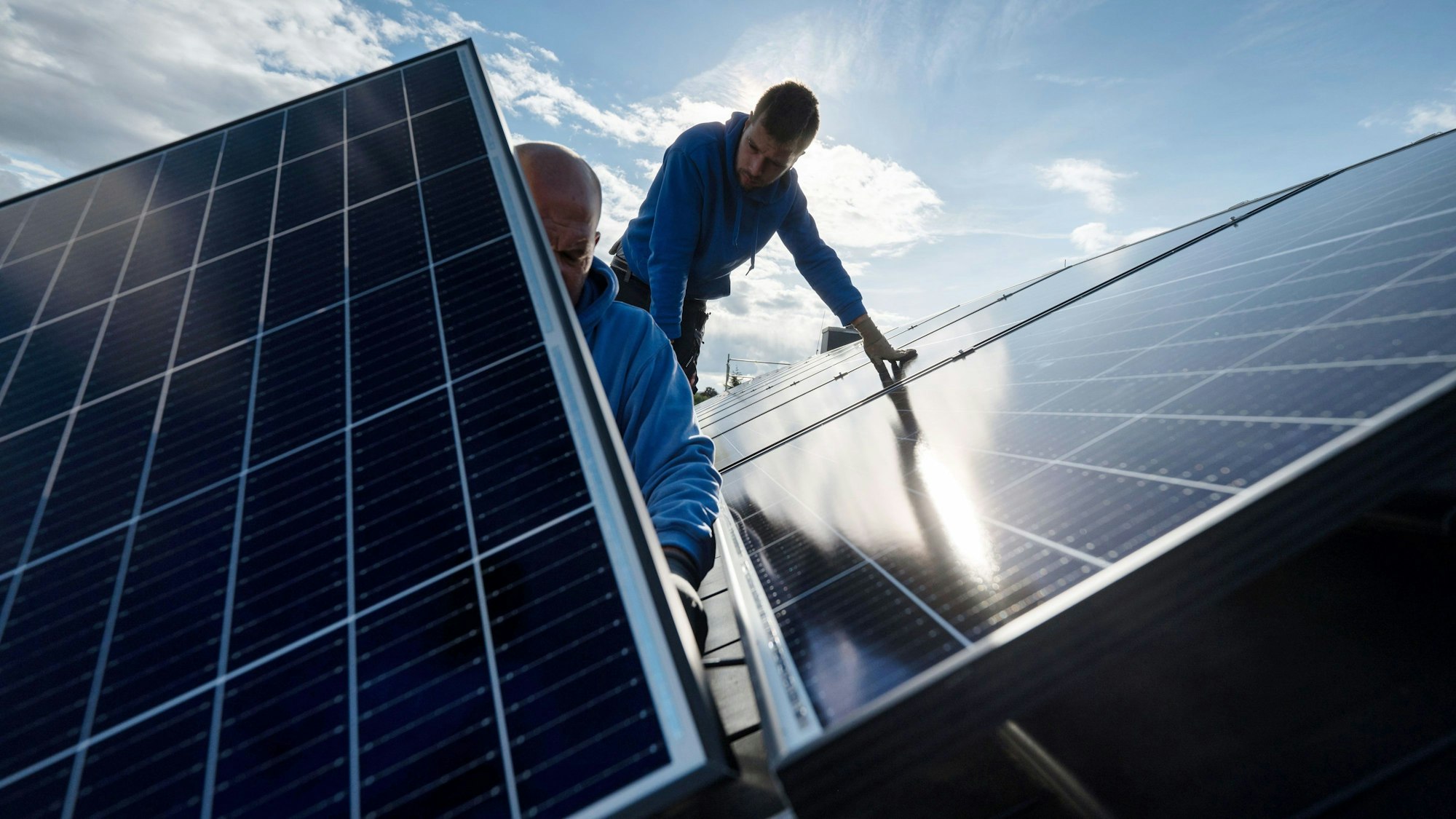 Arbeiter montieren Photovoltaikmodule auf dem Dach eines Wohnhauses.