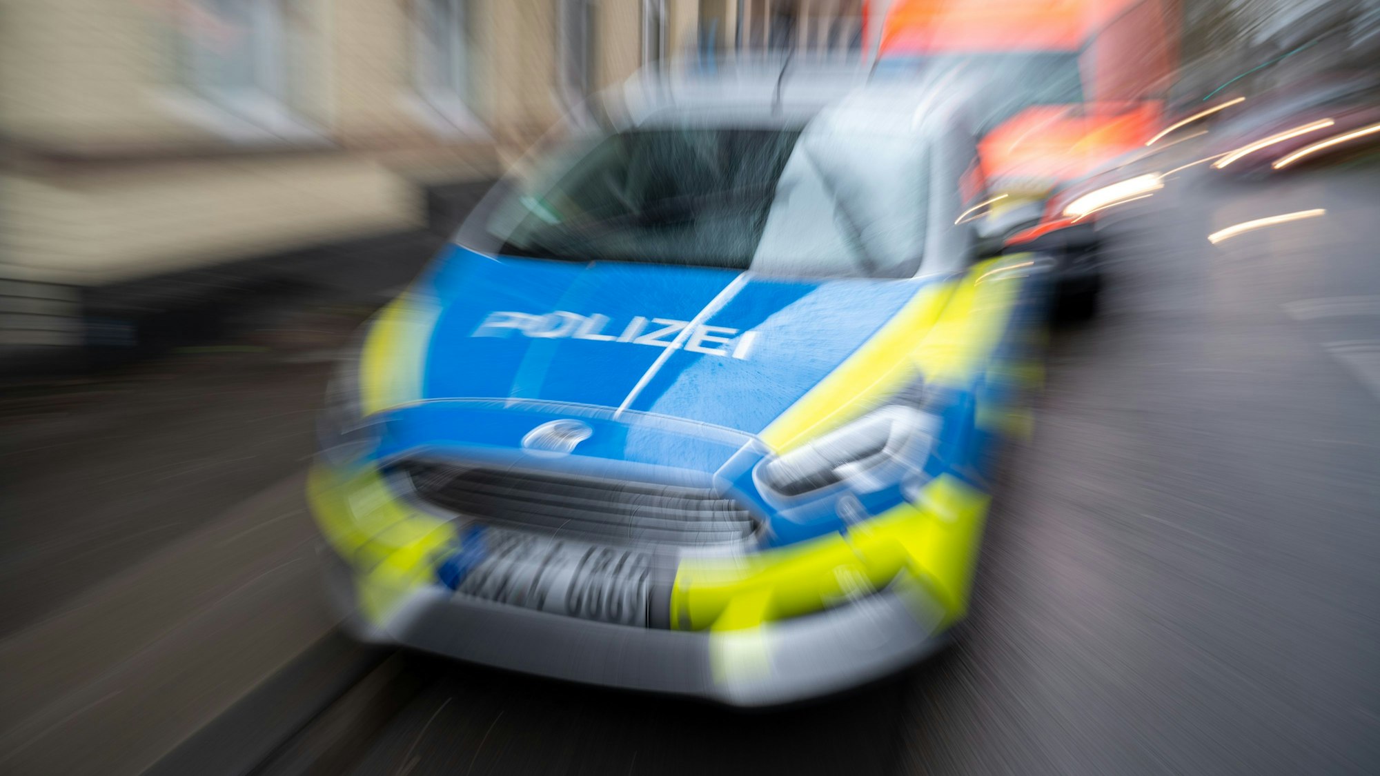 Ein Einsatzfahrzeug der Kölner Polizei fährt auf der Straße, dahinter ist ein Krankenwagen zu sehen.