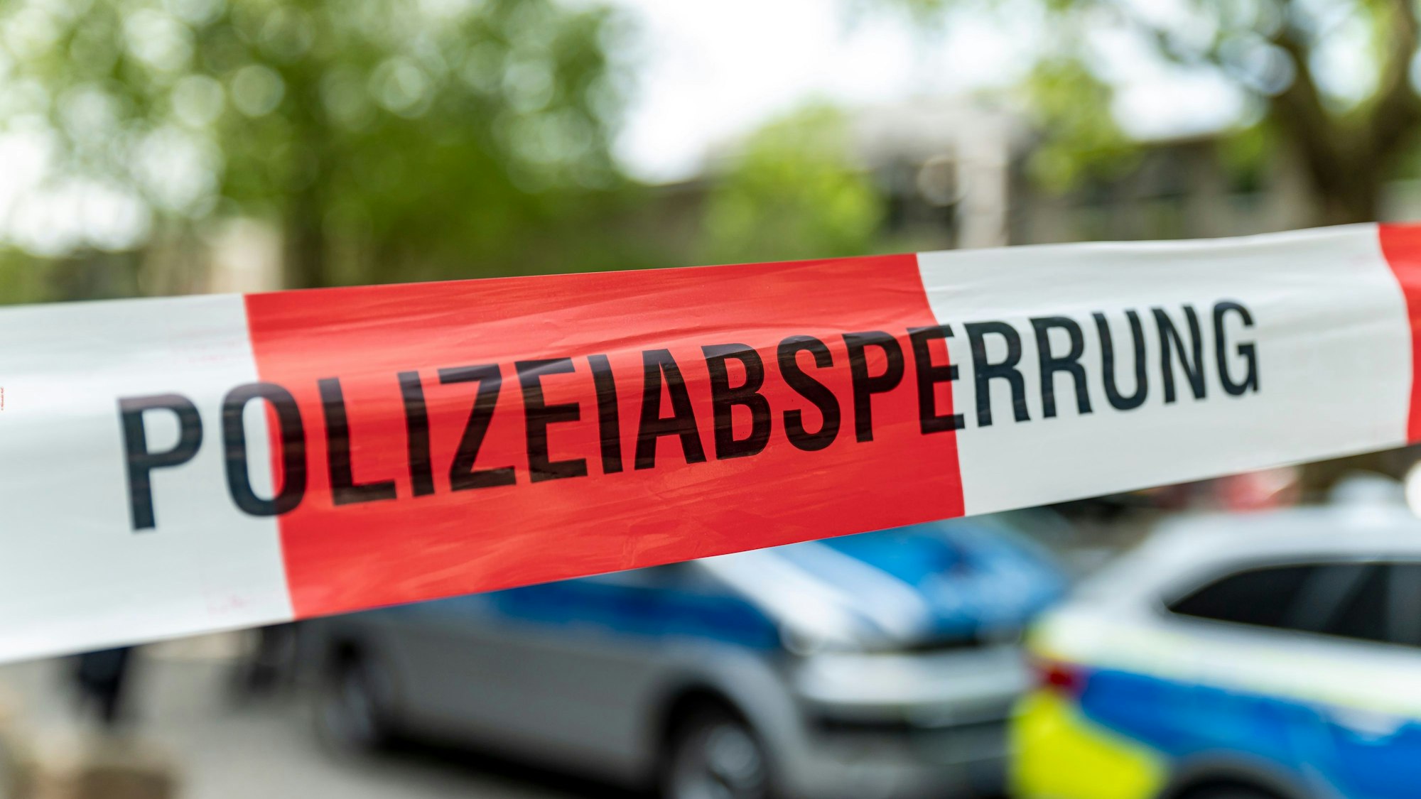 Polizeiabsperrband, dahinter stehen zwei Polizeifahrzeuge.