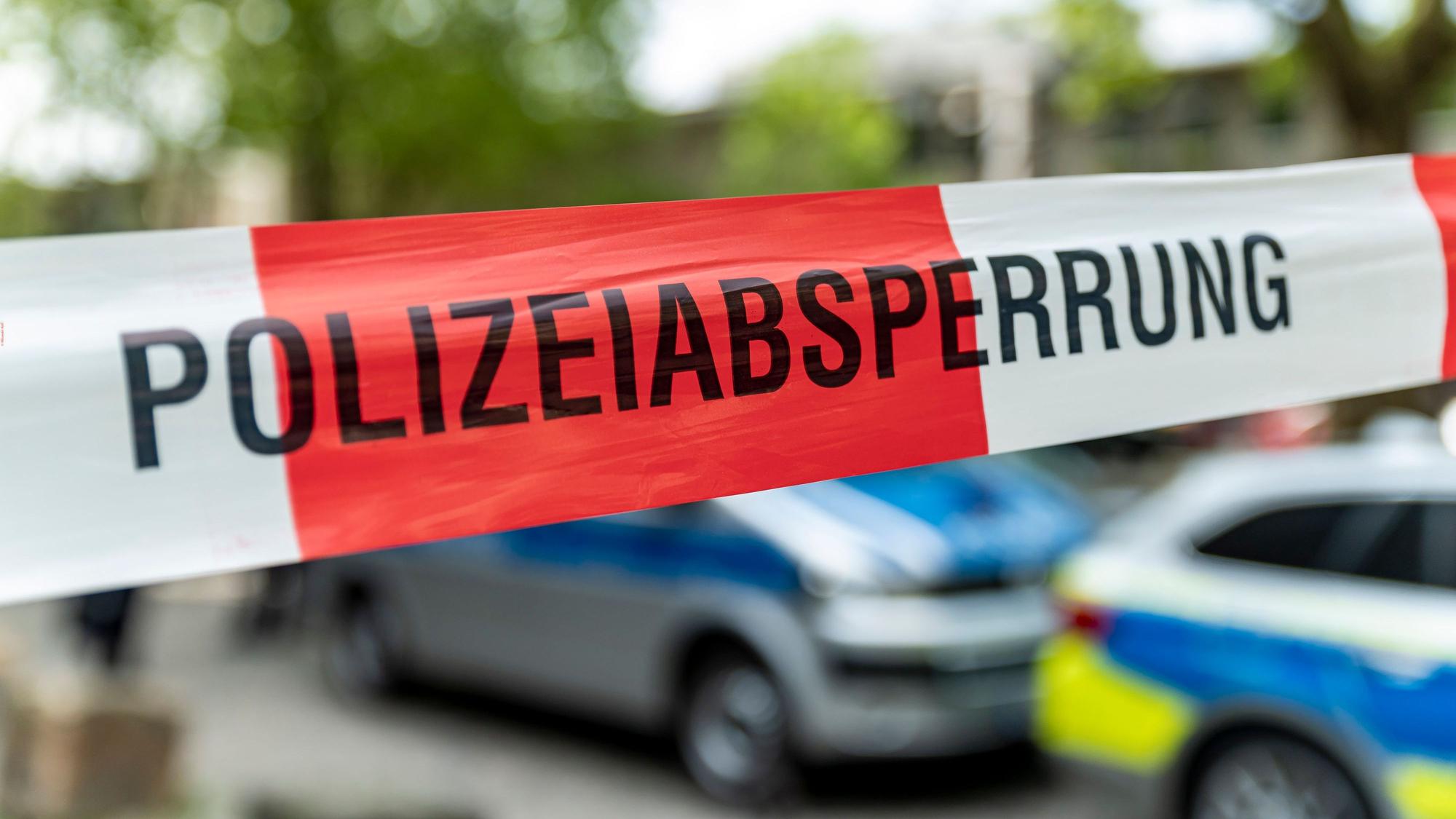 Ein Flatterband mit der Aufschrift „Polizeiabsperrung“ vor Polizeiautos.