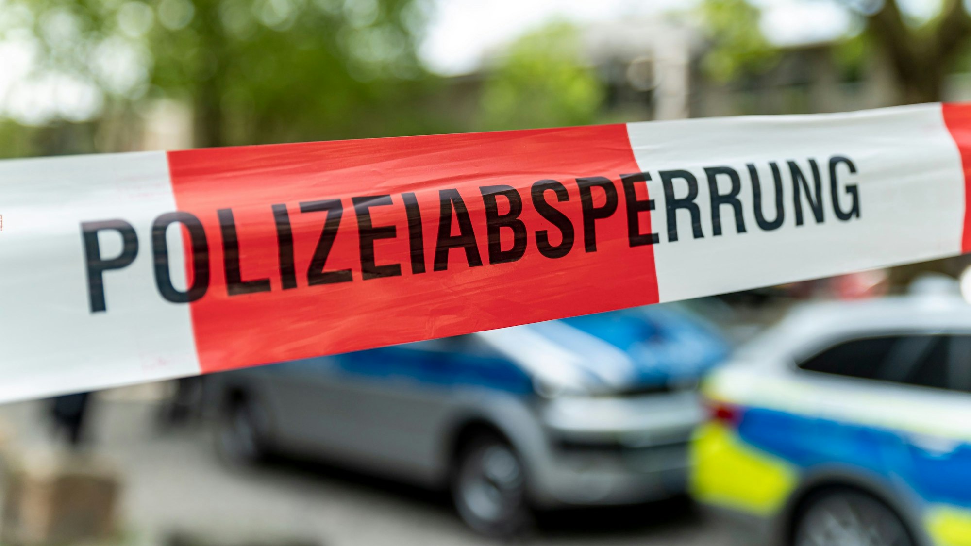 Ein Flatterband mit der Aufschrift „Polizeiabsperrung“ vor Polizeiautos.