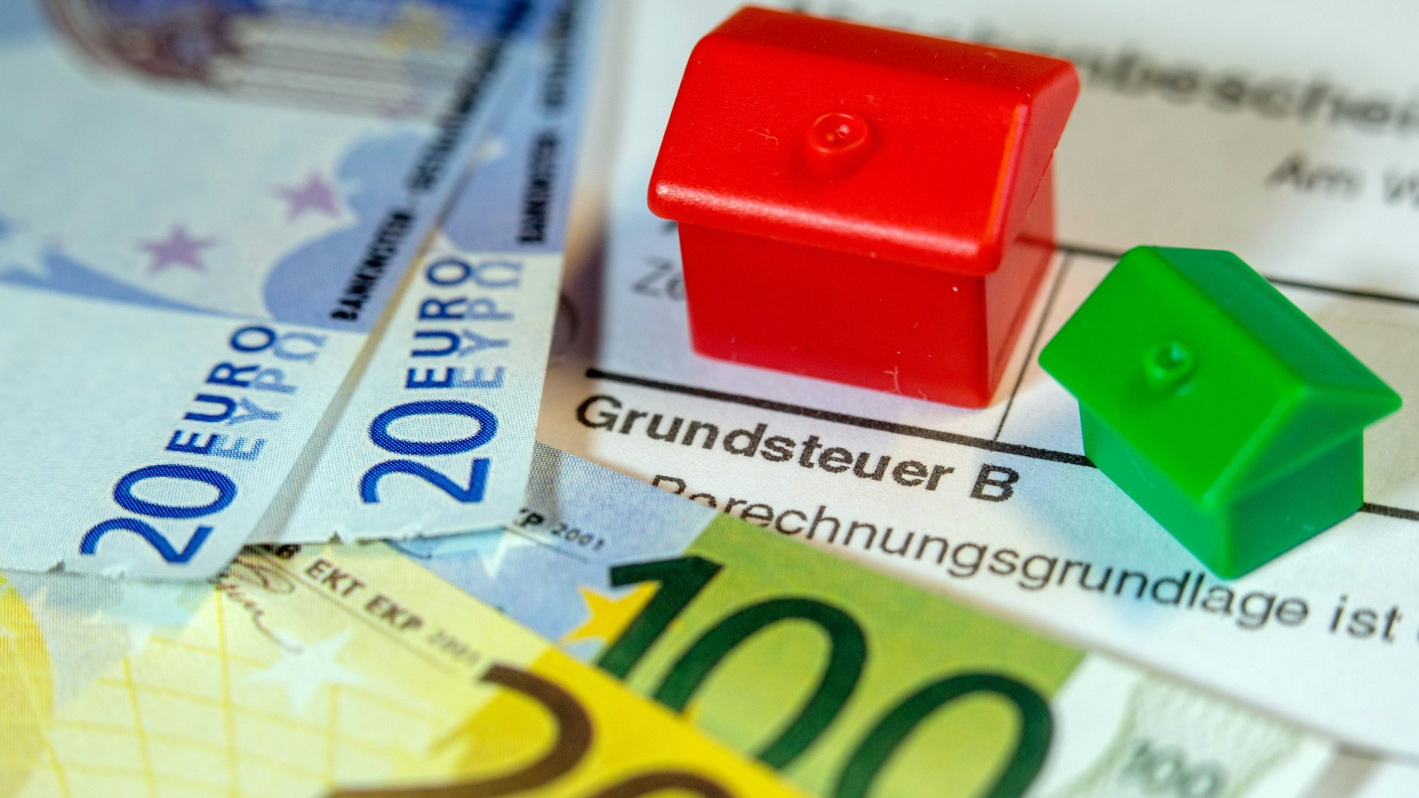 Ein Spielzeughaus und die Nachbildung von Euro-Geldscheinen liegen auf einem Abgabenbescheid für die Entrichtung der Grundsteuer.