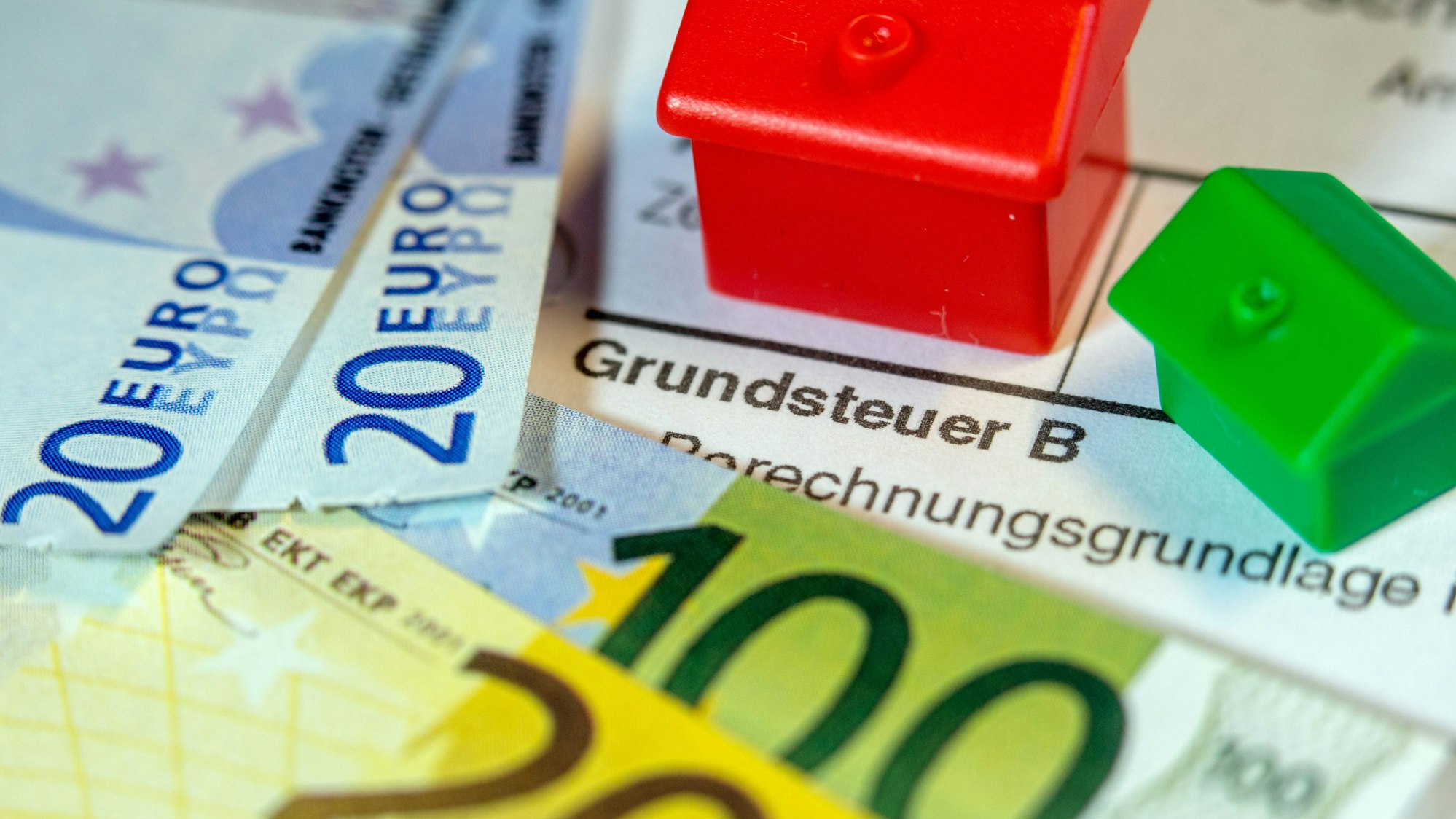 Zu sehen ist ein Formular zur Grundsteuer B, darauf Geldscheine und Spielzeughäuser.