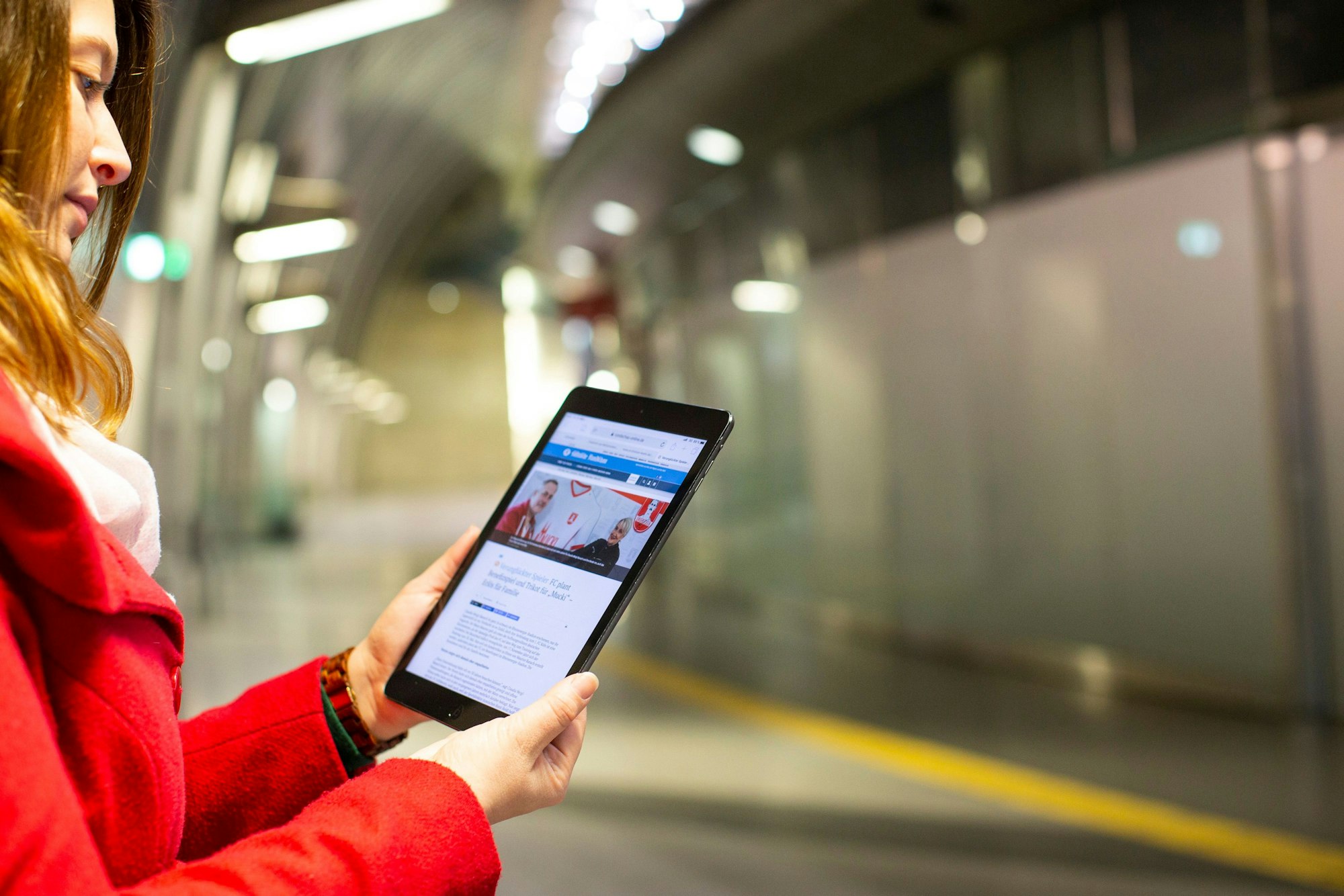 Eine junge Frau steht auf dem Bahnsteig und liest Nachrichten der Rundschau auf ihrem Tablet.