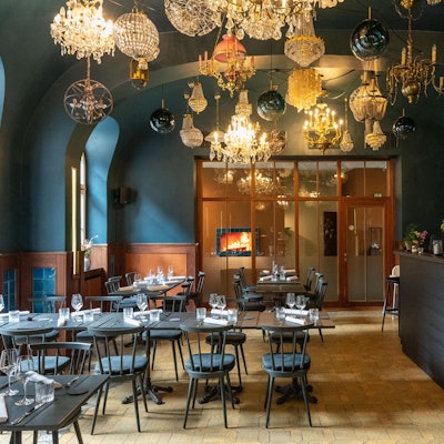 Graue Tische und Stühle in einem Raum mit dunklen Wänden und vielen Kronleuchtern an der Decke.