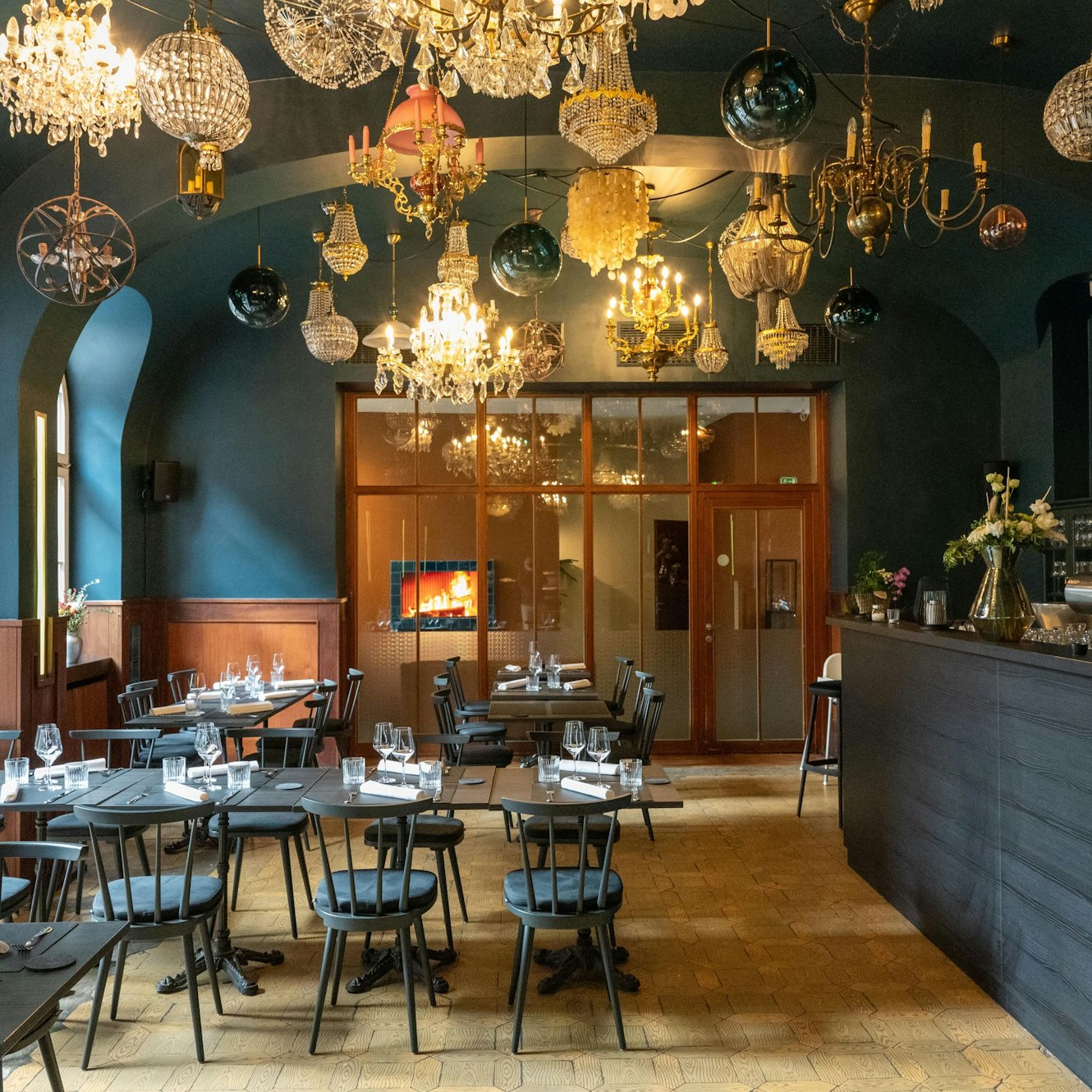 Graue Tische und Stühle in einem Raum mit dunklen Wänden und vielen Kronleuchtern an der Decke.