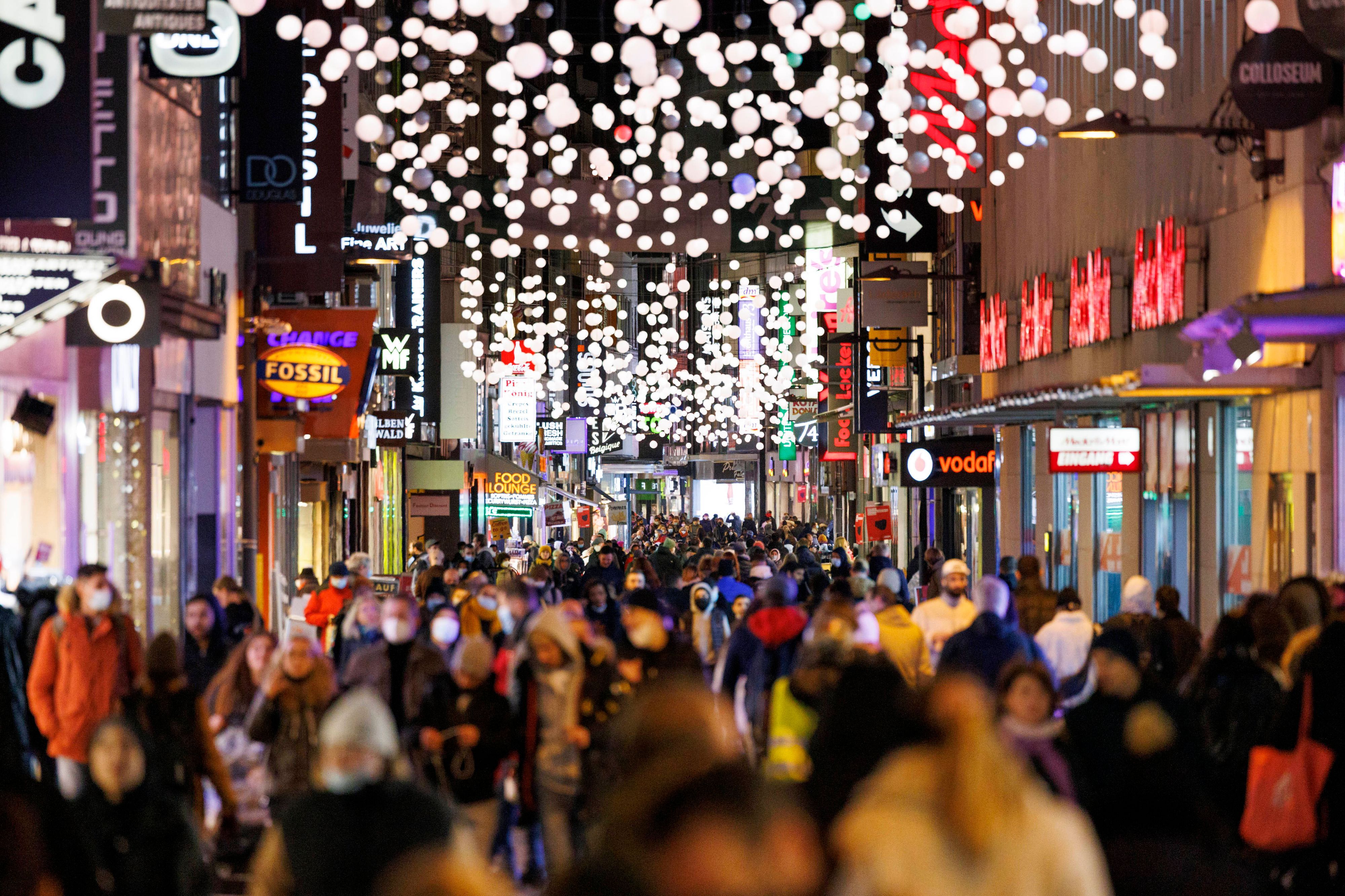 Passanten streifen durch die von Weihnachtsbeleuchtung gesäumte Hohe Straße in Köln.