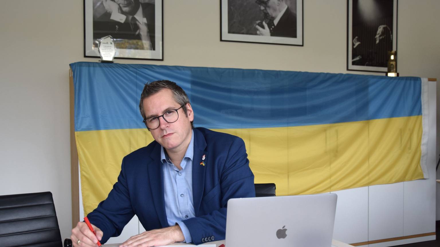 Bedburgs Bürgermeister Sascha Solbach unterzeichnet die Urkunde zur Solidaritätspartnerschaft mit Mykolajiw. Im Hintergrund ist eine Ukraine-Flagge zu sehen.