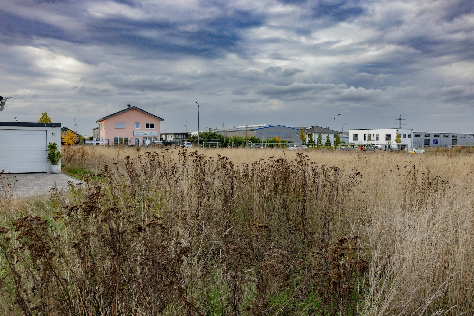 Ein freies Feld, an dessen Rand vereinzelt Gebäude stehen.