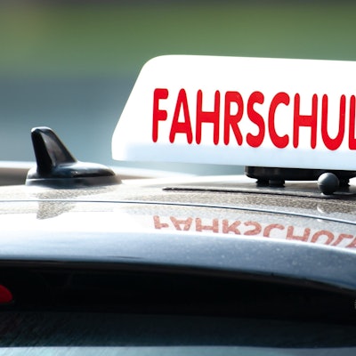 Ein weißes Fahrschul-Schild mit roter Aufschrift ist auf einem Autodach zu sehen.
