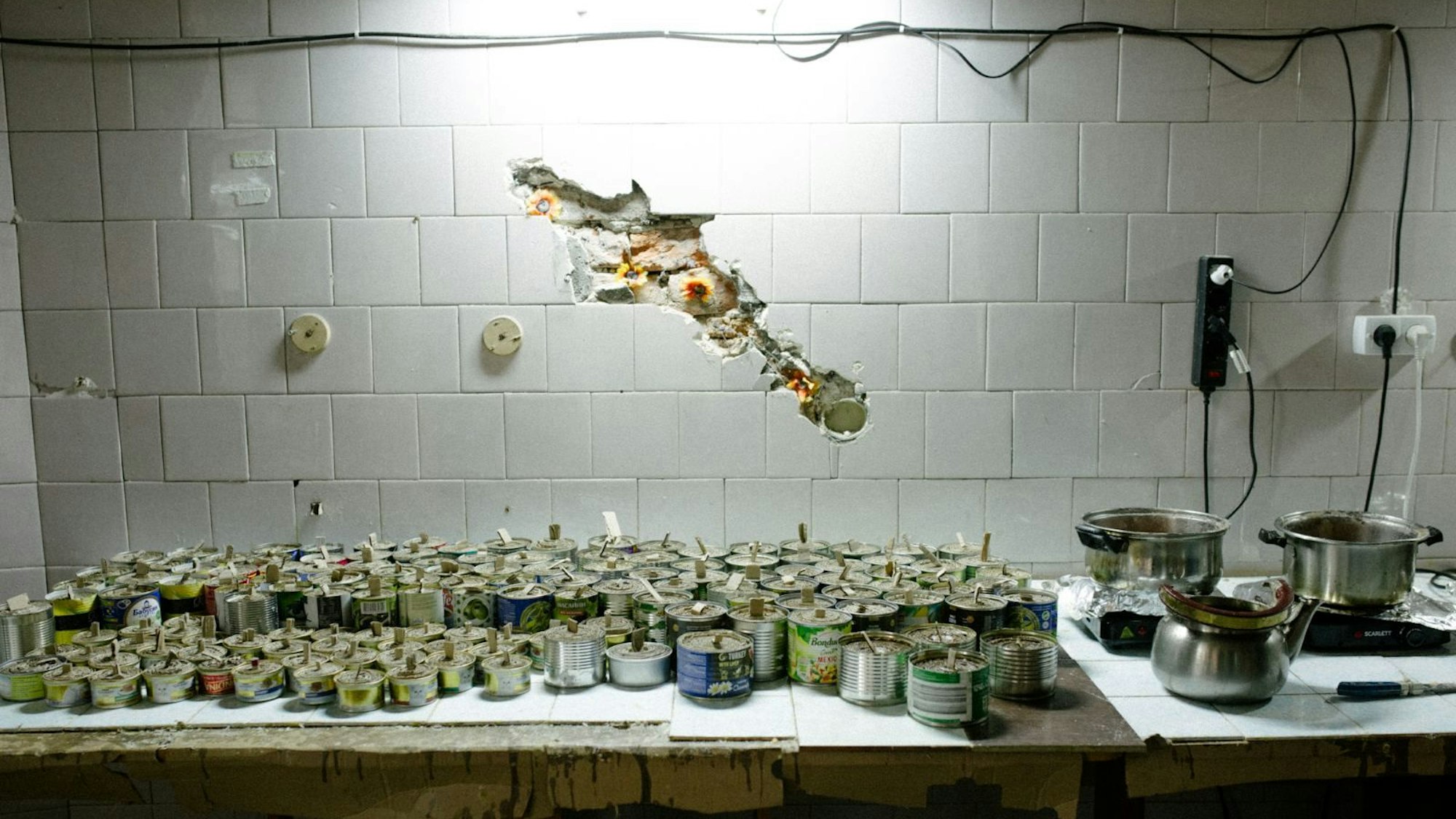 Kerzenreste stehen auf einem Tisch. Dahinter ist eine Wand, in der ein Loch ist.