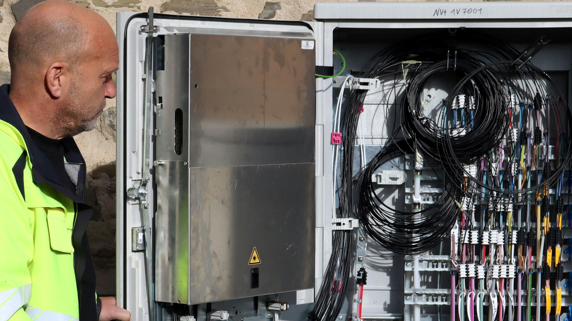 Ein offener Schaltkasten mit ganz vielen Kabeln und davor steht Rainer Braun.