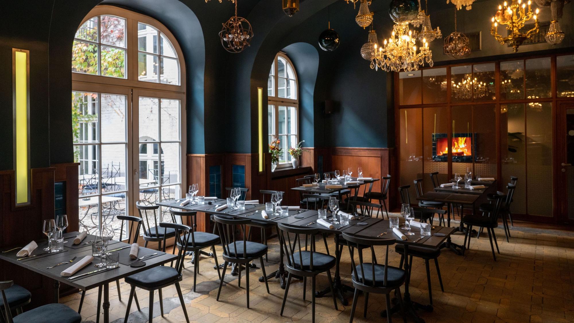 Innenraum des Restaurants „Augustin", Blick auf bondentiefe Fenster, von der Decke hängen viele verschiedene Lampen und Kronleuchter