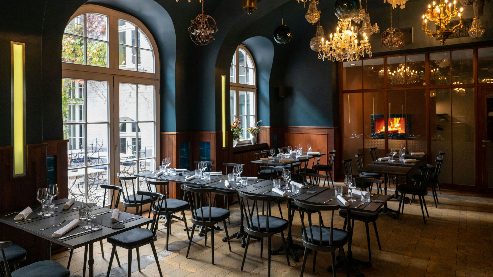 Innenraum des Restaurants „Augustin", Blick auf bondentiefe Fenster, von der Decke hängen viele verschiedene Lampen und Kronleuchter