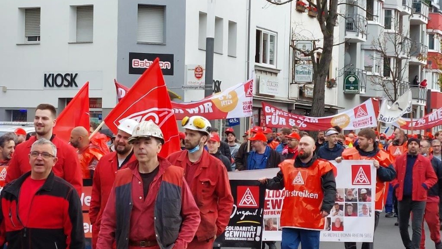 Demonstranten in roter Kleidung streiken für mehr Gehalt. Sie halten roten Fahnen in ihren Händen.