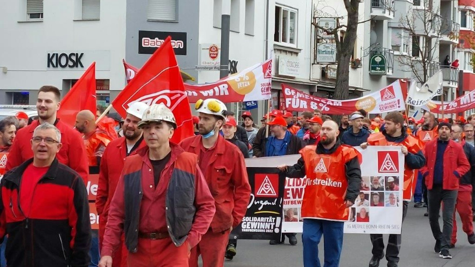 Demonstranten in roter Kleidung streiken für mehr Gehalt. Sie halten roten Fahnen in ihren Händen.