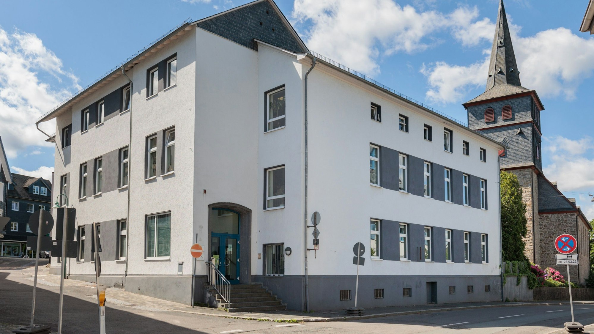 Das Bild zeigt ein weißes Gebäude, das Amtsgericht in Waldbröl. Im Hintergrund ist eine Kirche zu sehen.