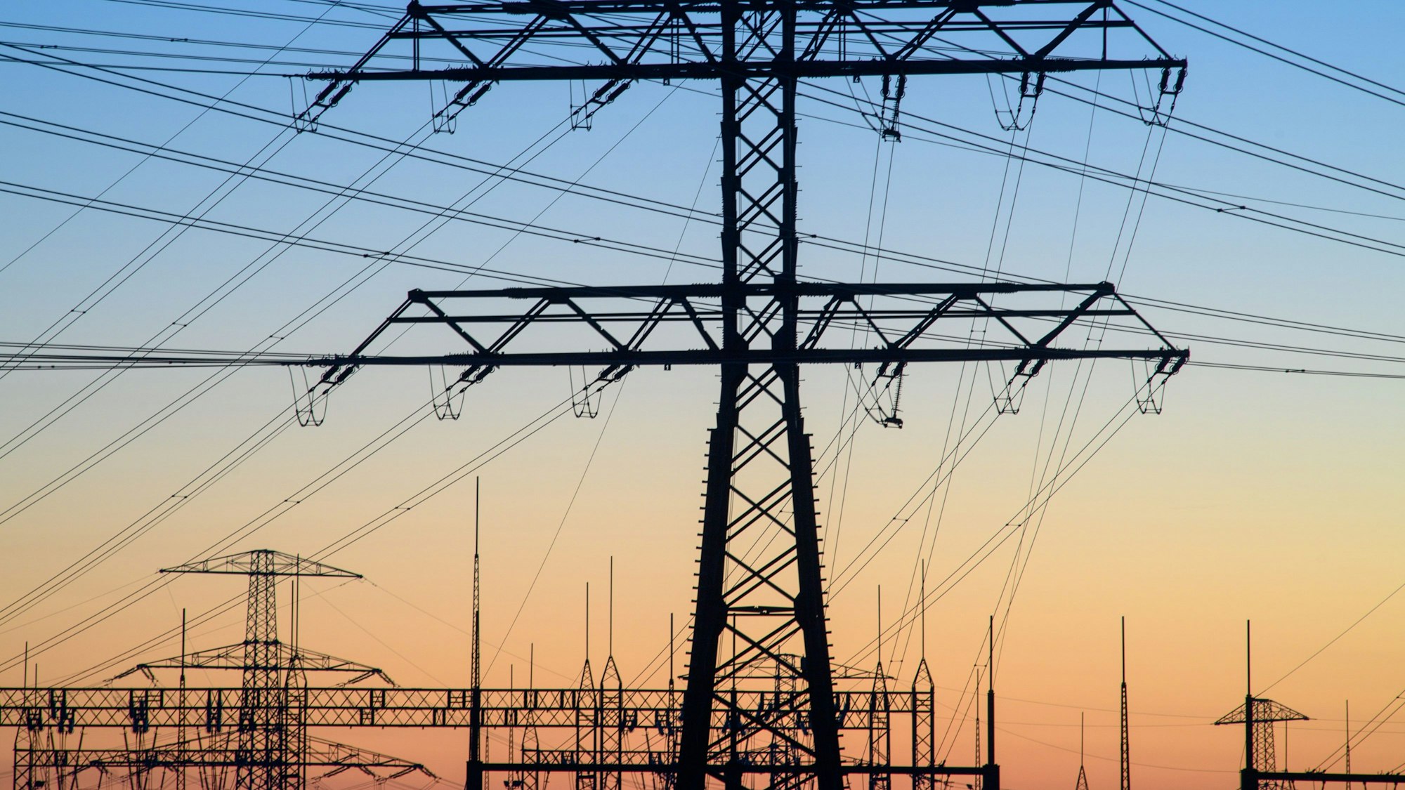 Der Morgen bricht über den Strommasten eines Umspannwerks an.