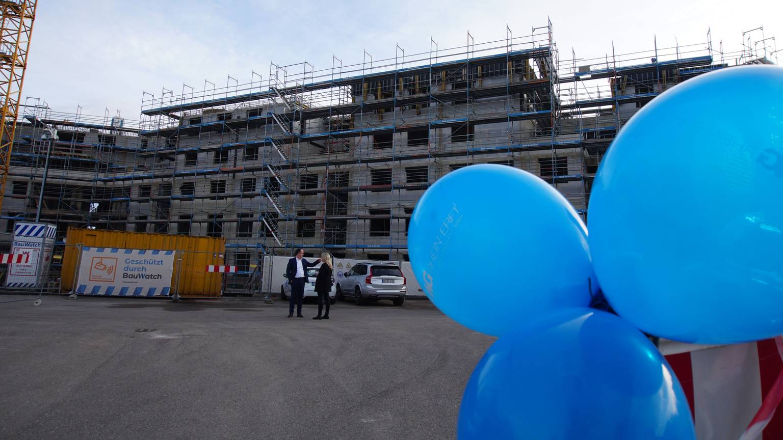 Blaue Luftballons schweben vor einem Rohbau.