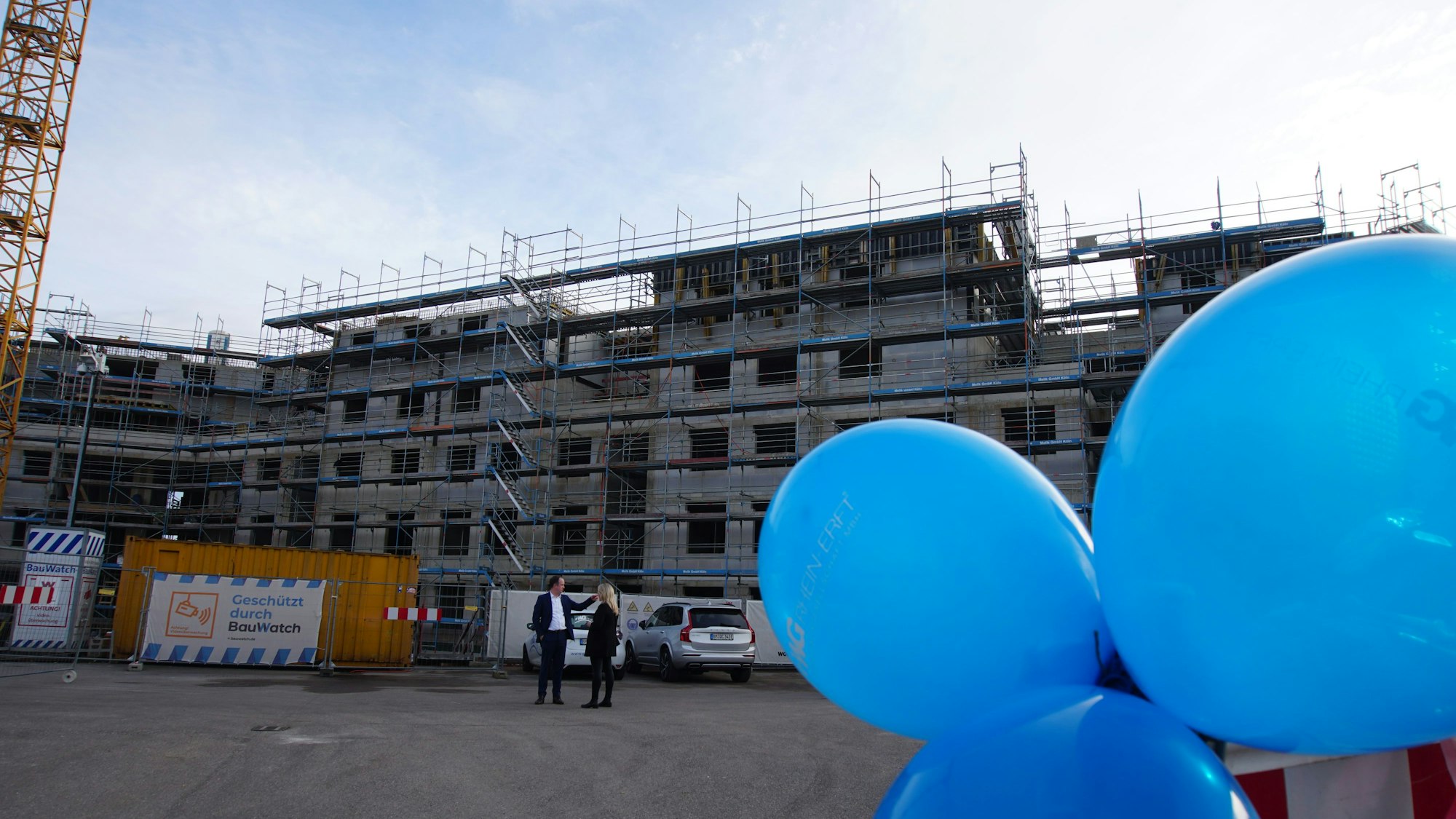 Blaue Luftballons schweben vor einem Rohbau.