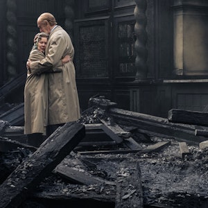 Netflix' „The Crown“-Darsteller Imelda Staunton und Jonathan Pryce umarmen sich in einem verkohlt aussehendem Raum.