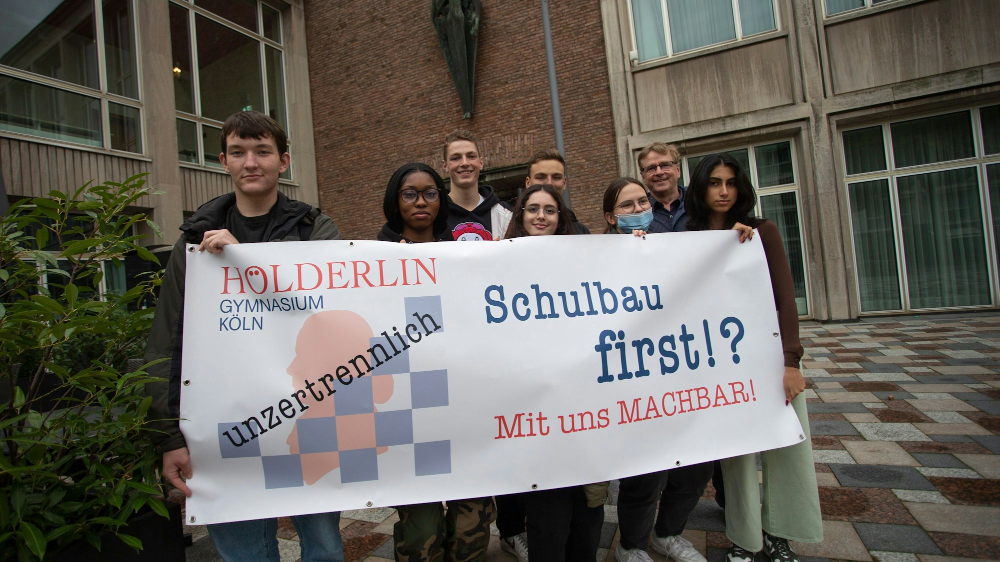 Schüler halten ein Plakat hoch, auf dem „Schulbau first!? Mit uns machbar!“ zu lesen ist.
