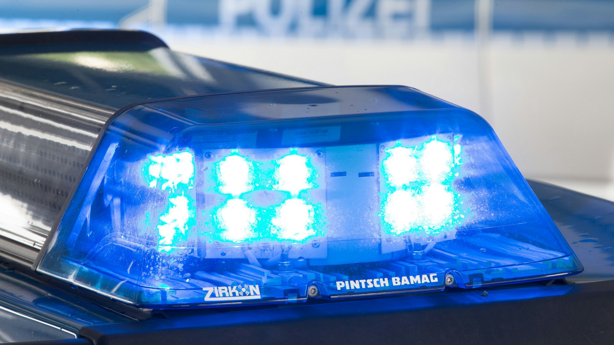 Eine Blaulicht leuchtet auf dem Dach eines Polizeiwagens. Im Hintergrund steht ein weiterer Streifenwagen.