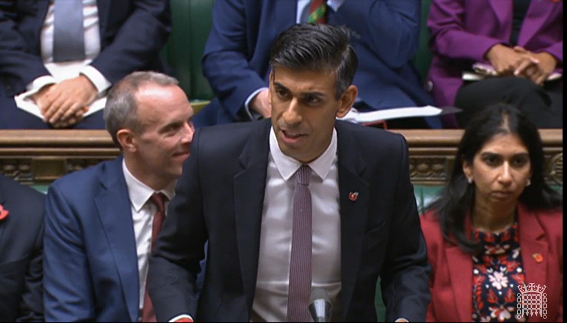 Premierminister Rishi Sunak ist in der Mitte des Bildes zu sehen. Mehrere Menschen sitzen im Hintergrund.