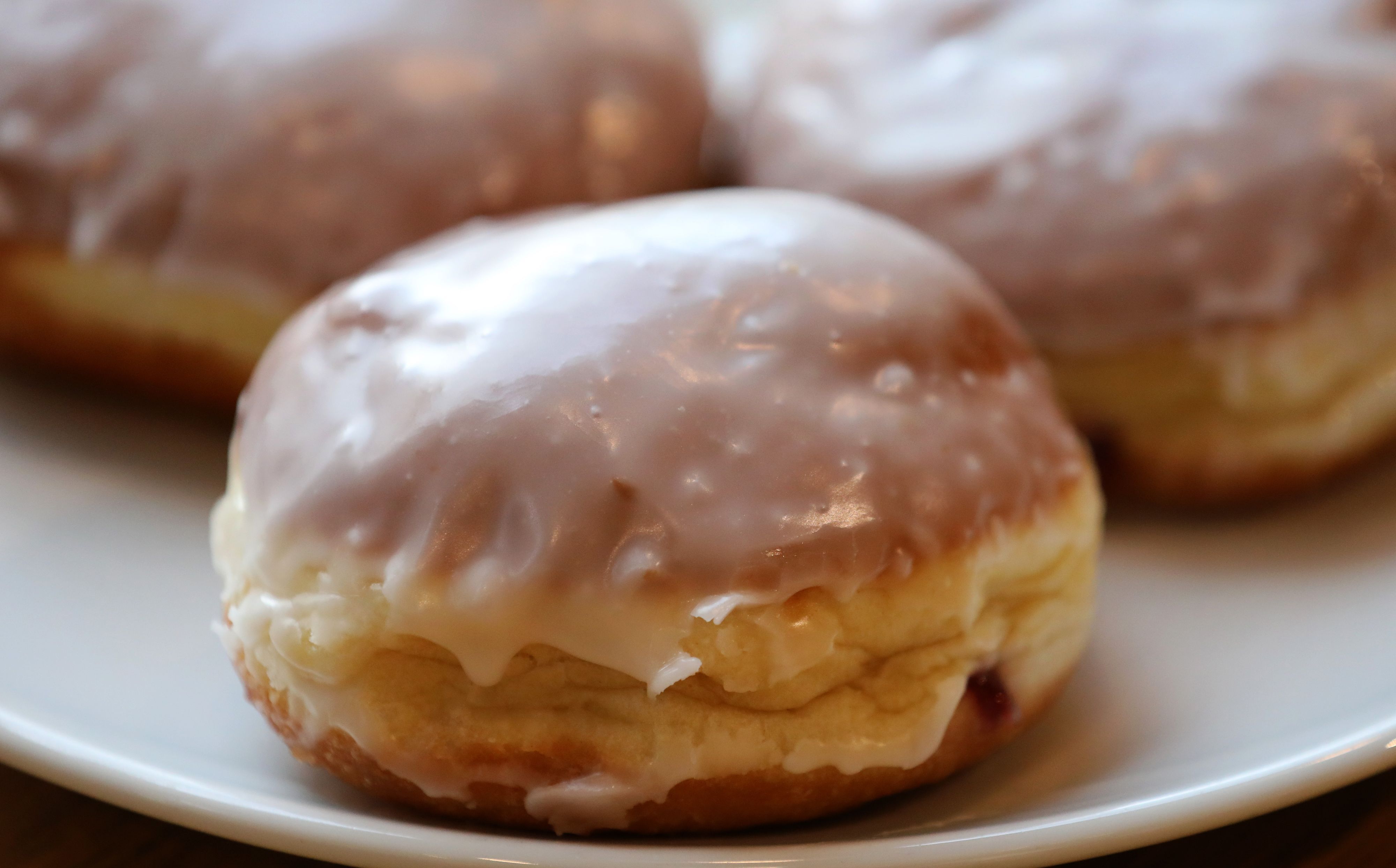 Ein Berliner bzw. Pfannkuchen liegt bei einem Bäcker auf einem Teller. Er ist mit Zuckerglasur überzogen (Symbolbild)