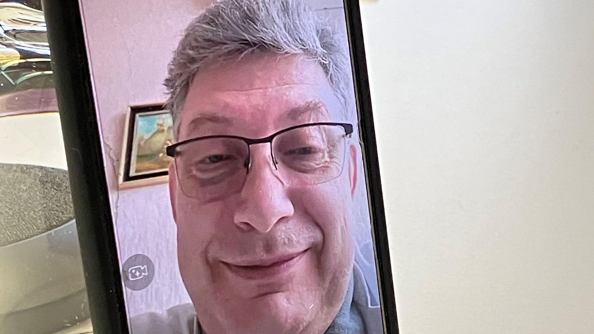 Dr. Vitaliy P., Arzt aus Charkiw, ist im Rahmen eines Videotelefonats auf einem Handybildschirm zu sehen.