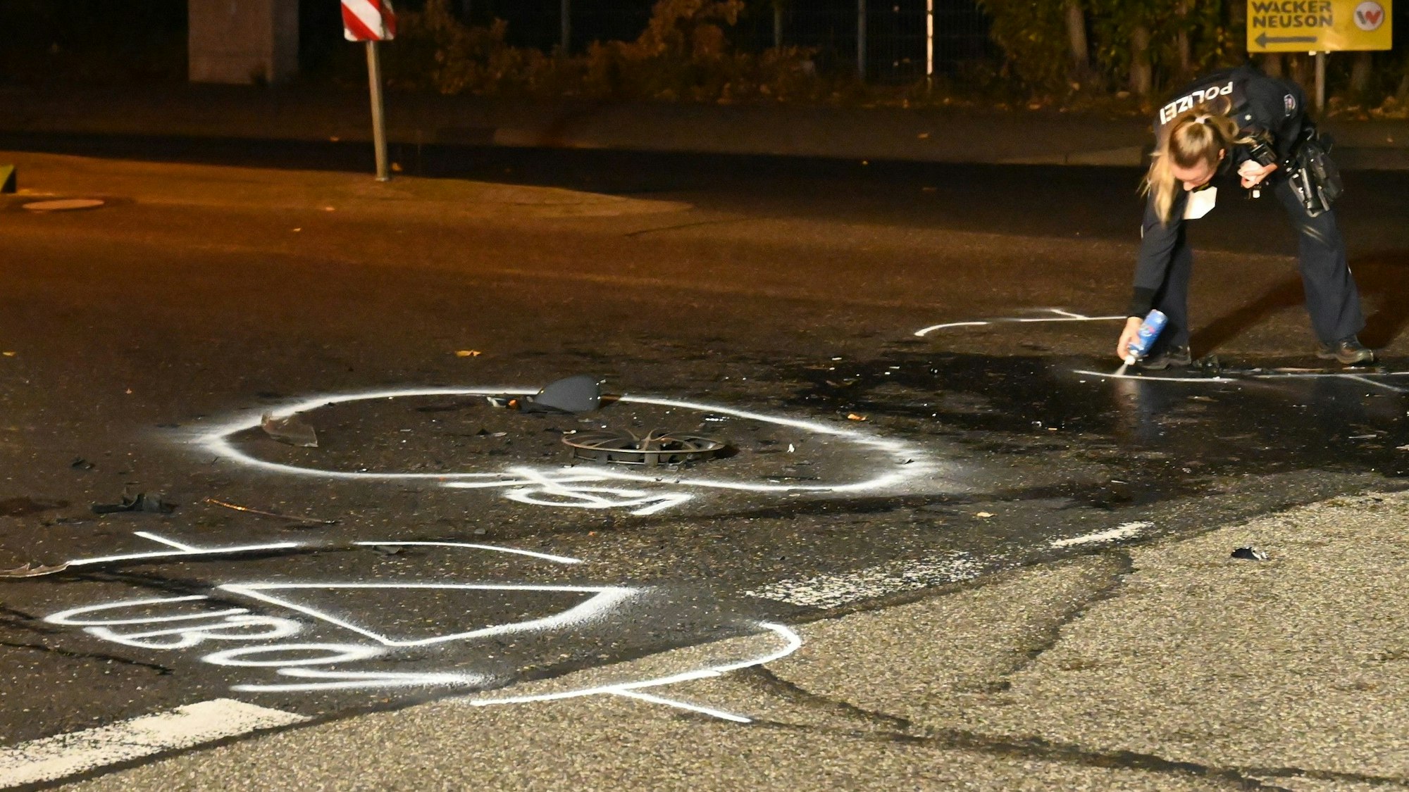 Eine Polizistin markiert auf der Straße mithilfe einer Sprühdose Stellen, auf denen Autoteile liegen.