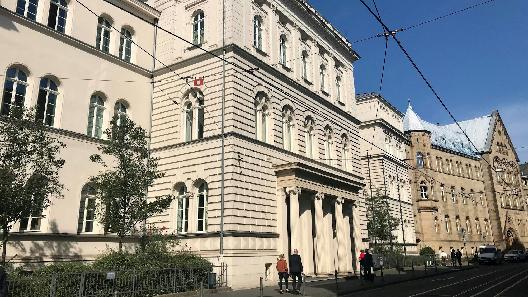 Außenansicht vom Landgericht Bonn. Bei schönem Wetter gehen vor dem Gebäude mehrere Personen spazieren.