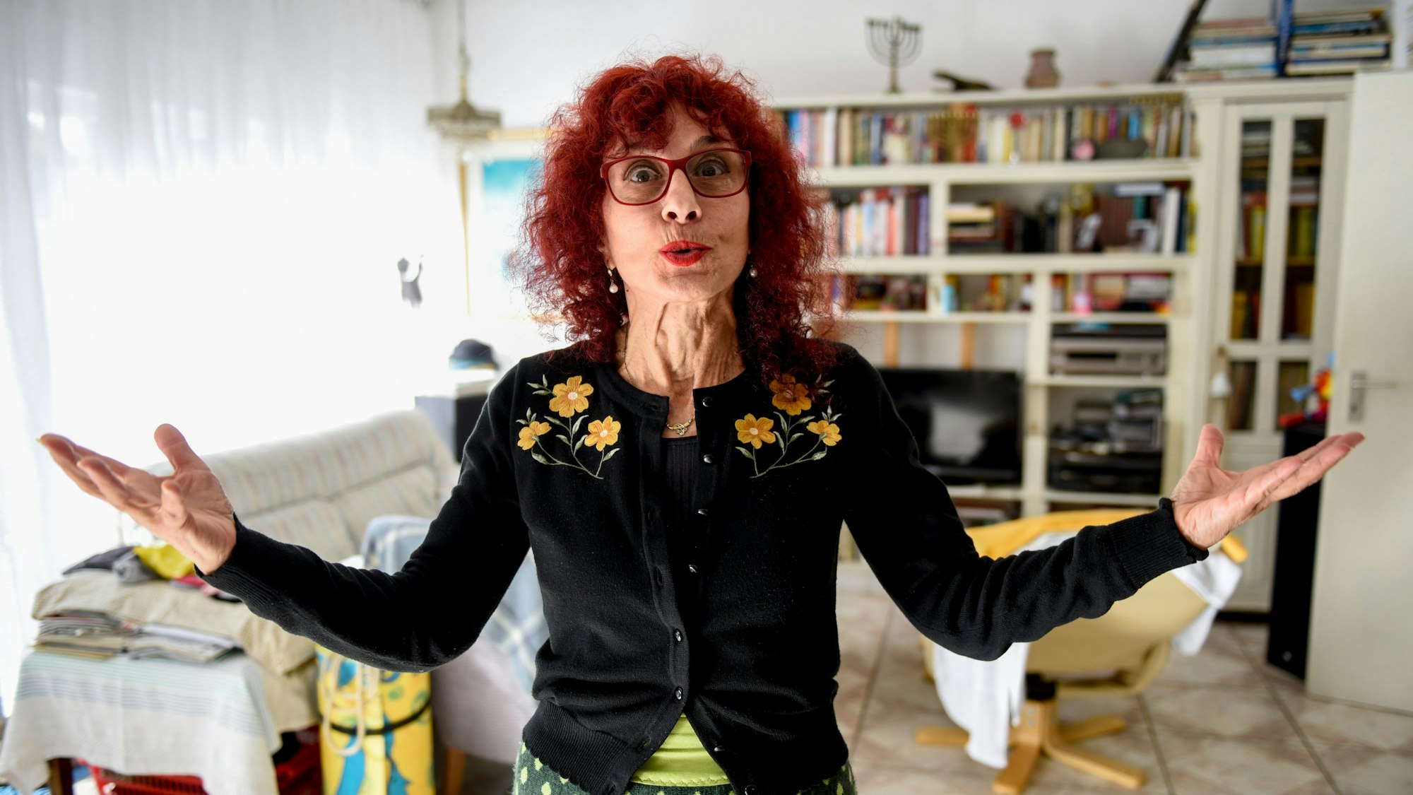 Shulamit Grohmann steht in ihrem Wohnzimmer, spitzt den Mund und hebt die Hände.