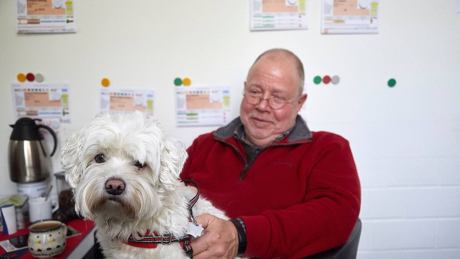 Rolf Zimmermann sitz auf einem Stuhl und hat einen Hund auf dem Schoß.