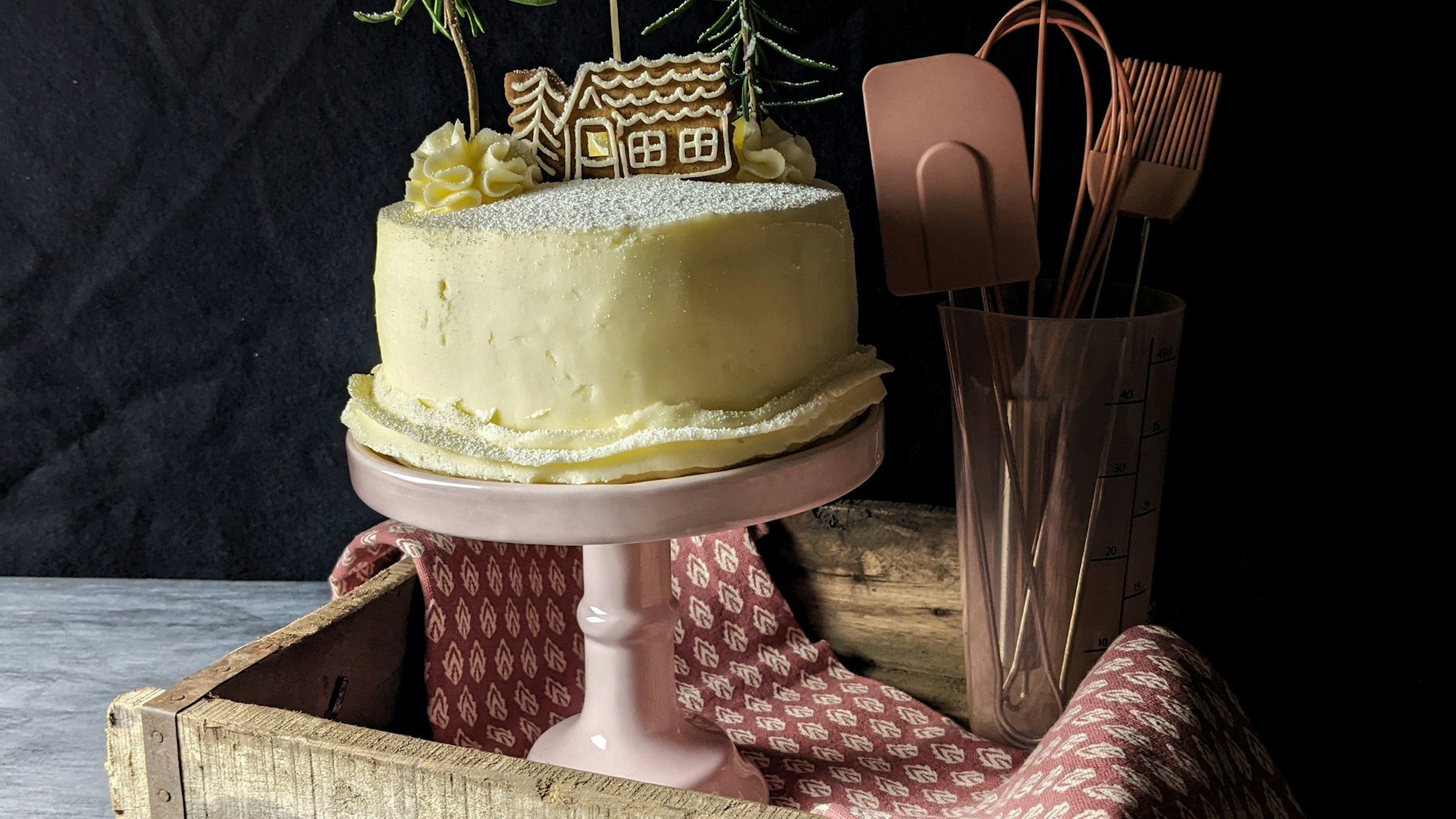 Zum Themendienst-Bericht von Doreen Hassek vom 9. November 2022: Die mit Buttercreme eingestrichene Weihnachtstorte bekommt als Deko einen Spekulatius und zwei Rosmarinzweige und sieht damit wie eine Winterlandschaft aus.