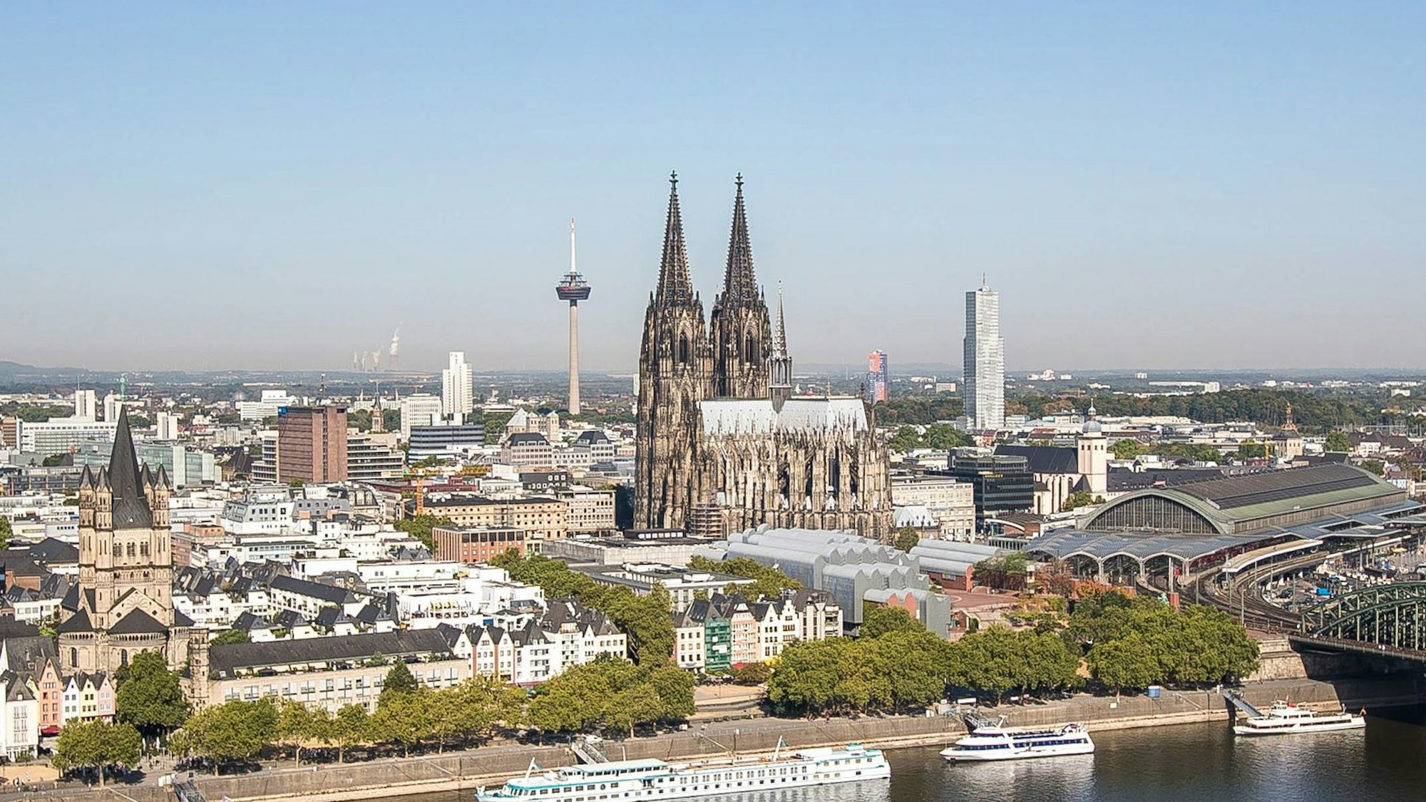 Köln mit Dom, Hohenzollernbrücke, Rhein und Hauptbahnhof bei strahlend blauem Himmel.