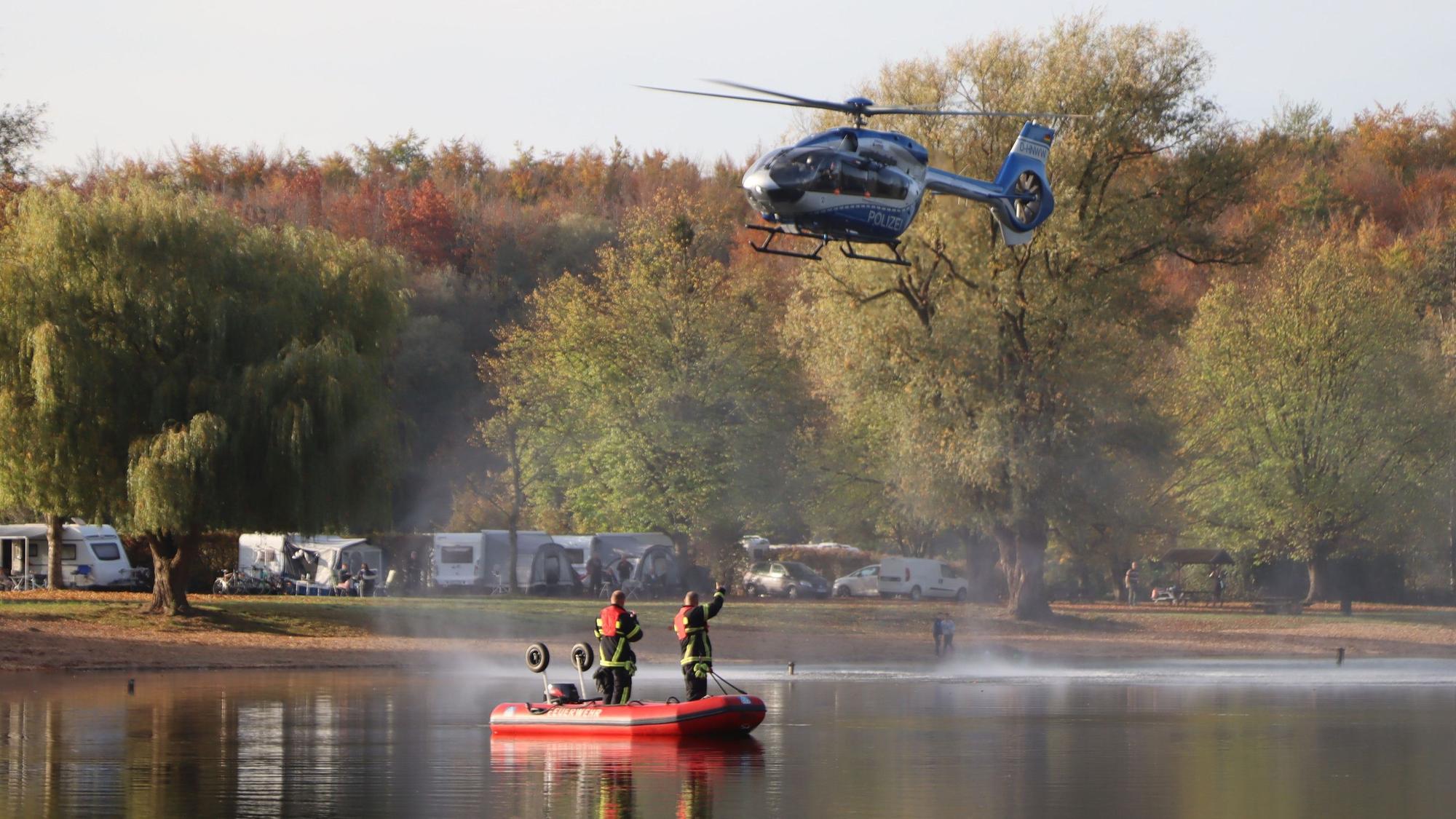 Feuerwehrleute in einem Rettungsboot auf einem See, über ihnen fliegt ein Hubschrauber.