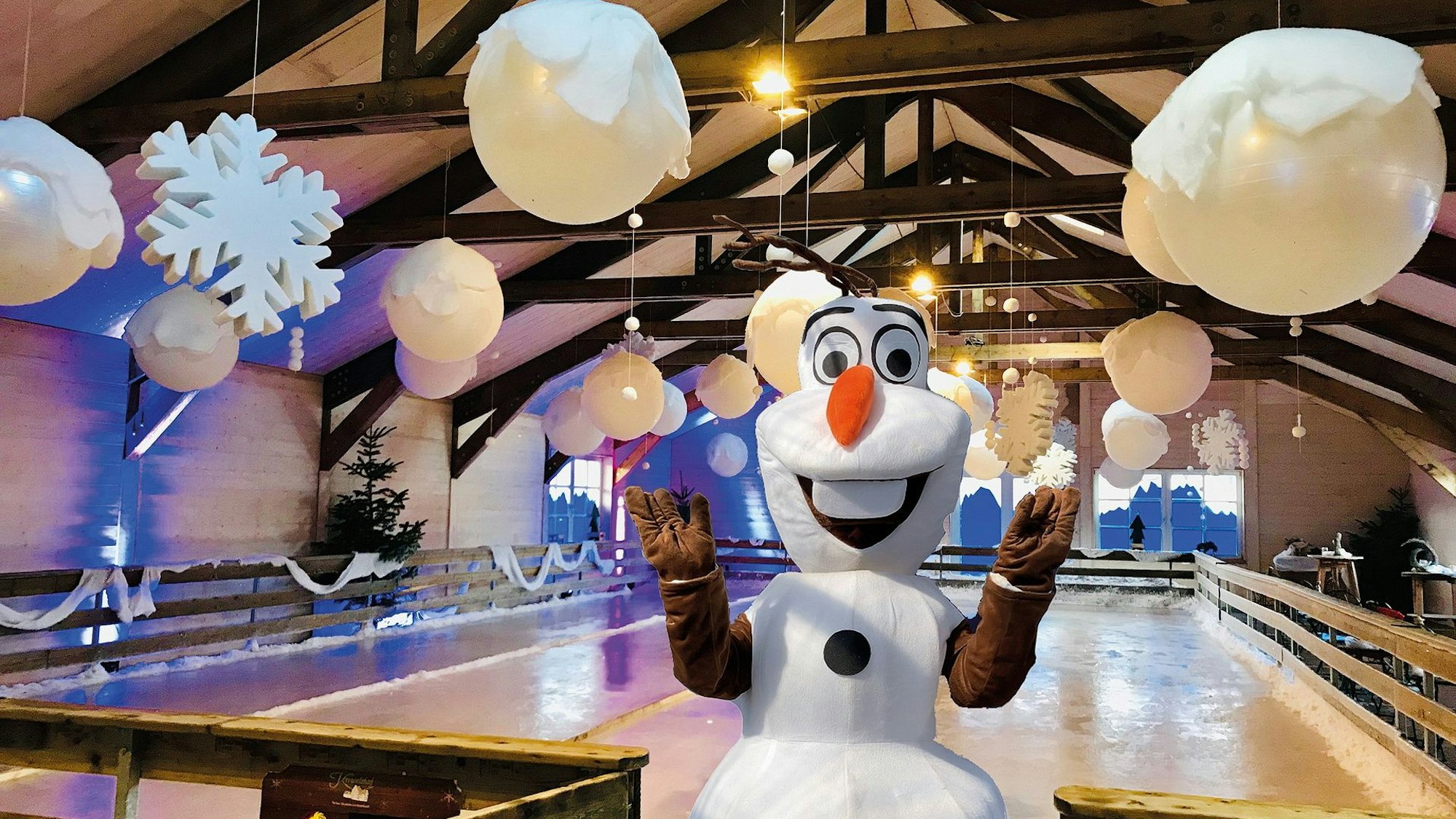 Olaf der Schneemann steht vor der Eisbahn des Krewelshofs, die winterlich mit Schnee und Eiskristallen dekoriert ist.