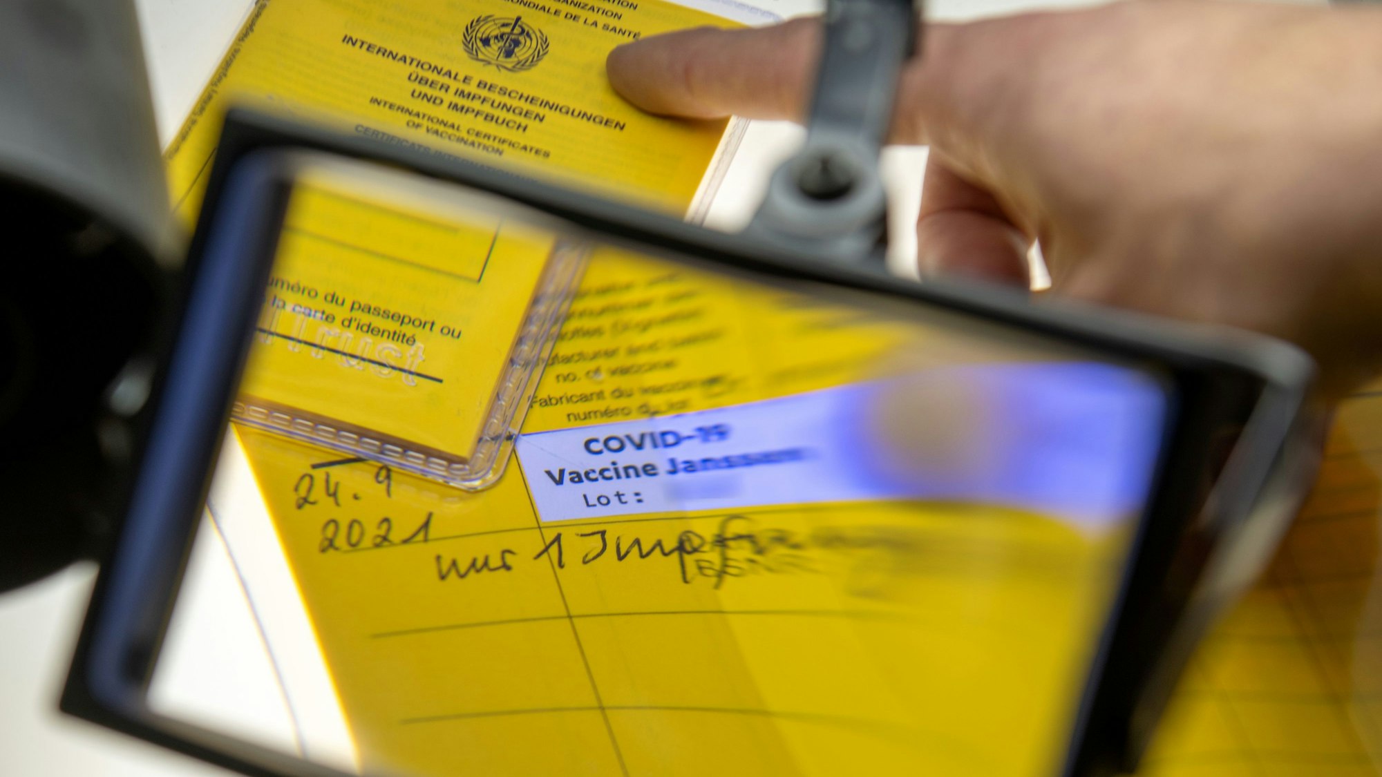 Ein aufgeschlagener Impfausweis mit dem Eintrag einer Corona-Impfung mit dem Impfstoff Johnson & Johnson wird unter einer Lupe betrachtet.