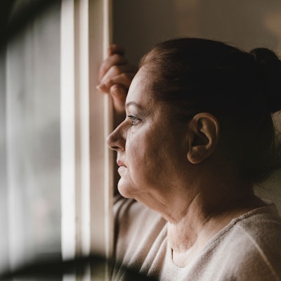 Deprimierte ältere Frau blickt sorgenvoll aus dem Fenster.