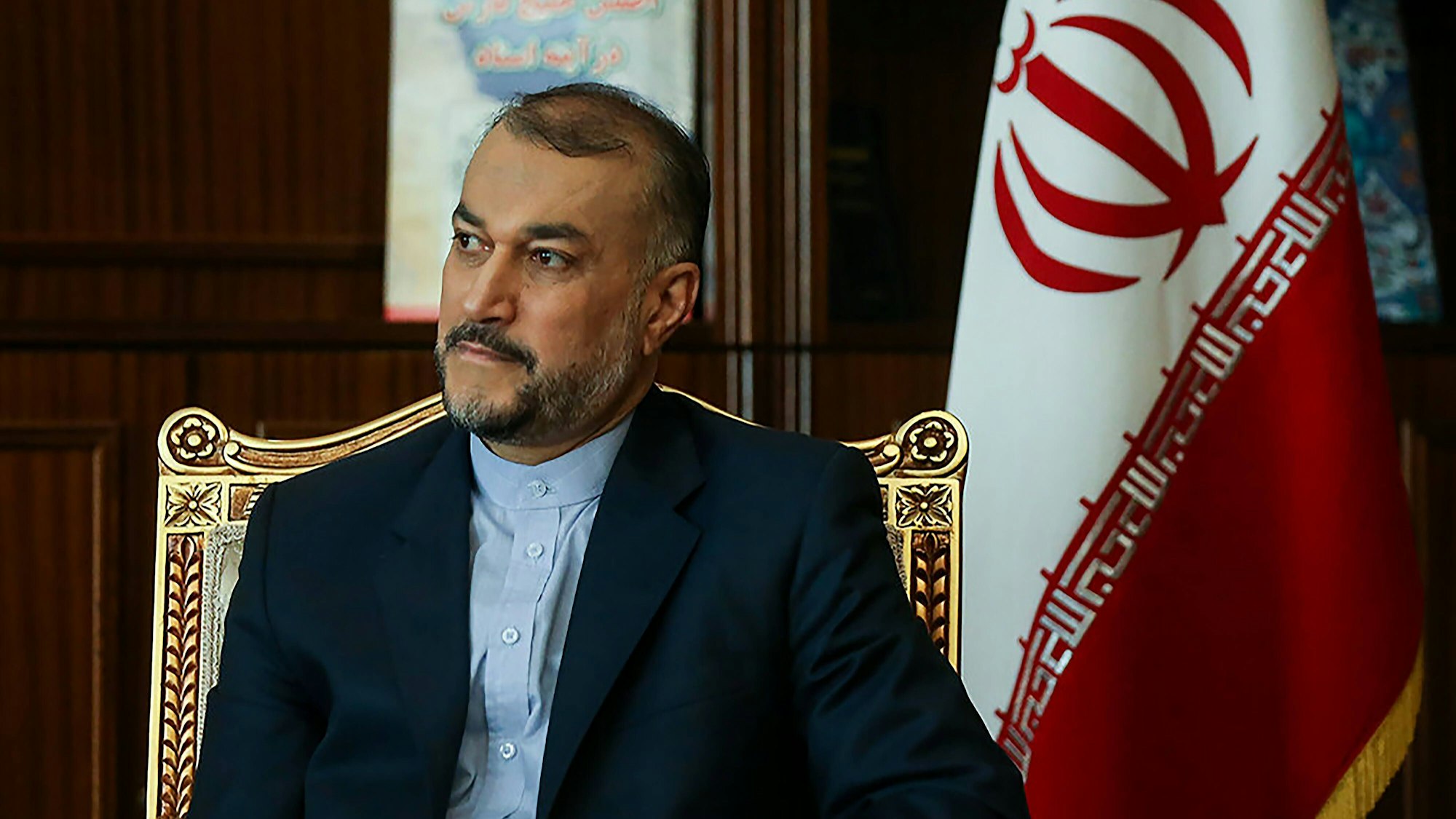Hossein Amir-Abdollahian, iranischer Außenminister, sitzt auf einem goldenen Stuhl, im Hintergrund ist eine iranische Fahne zu sehen.