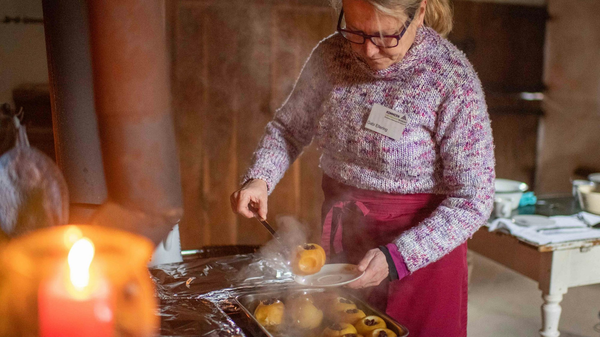 Eine Frau hebt einen dampfenden Bratapfel auf einen Teller.