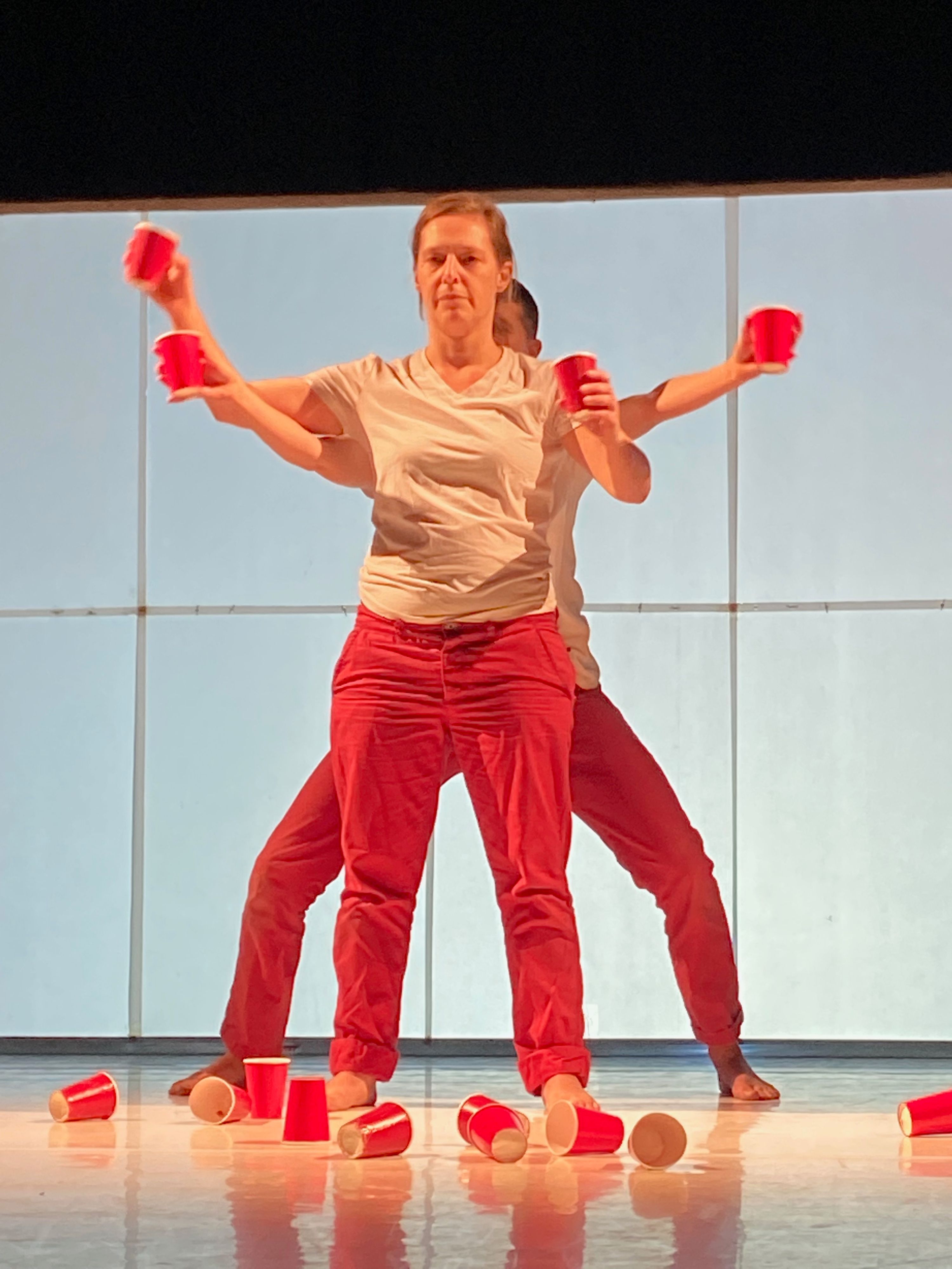 Zwei Mitglieder der "performing group" greifen in ihrer Darstellung auf der Bühne mit roten Einwegbechern das Thema Konsum kritisch auf.