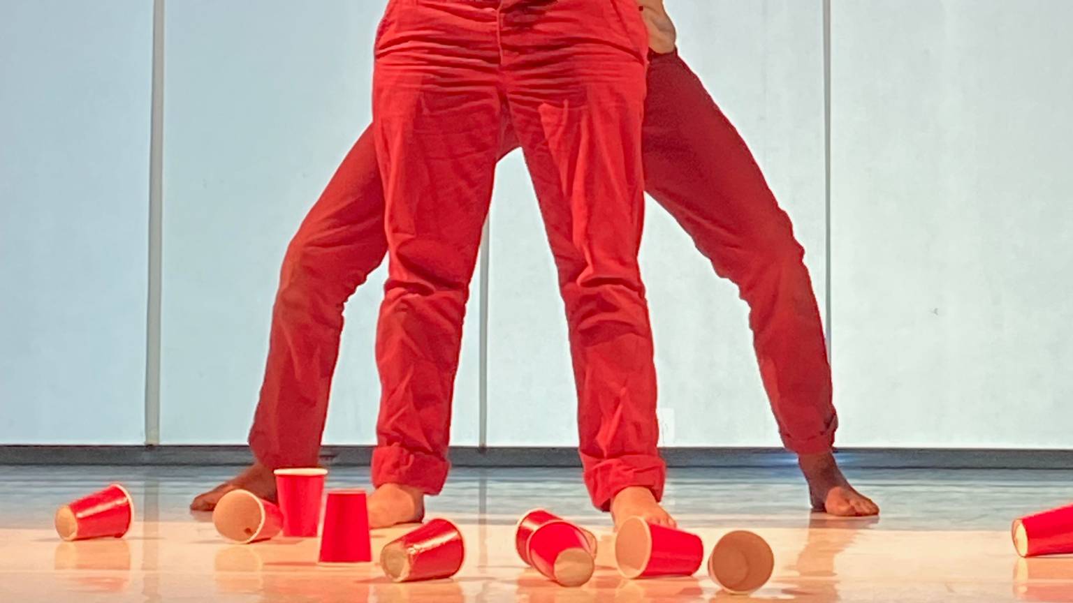 Zwei Mitglieder der "performing group" greifen in ihrer Darstellung auf der Bühne mit roten Einwegbechern das Thema Konsum kritisch auf.
