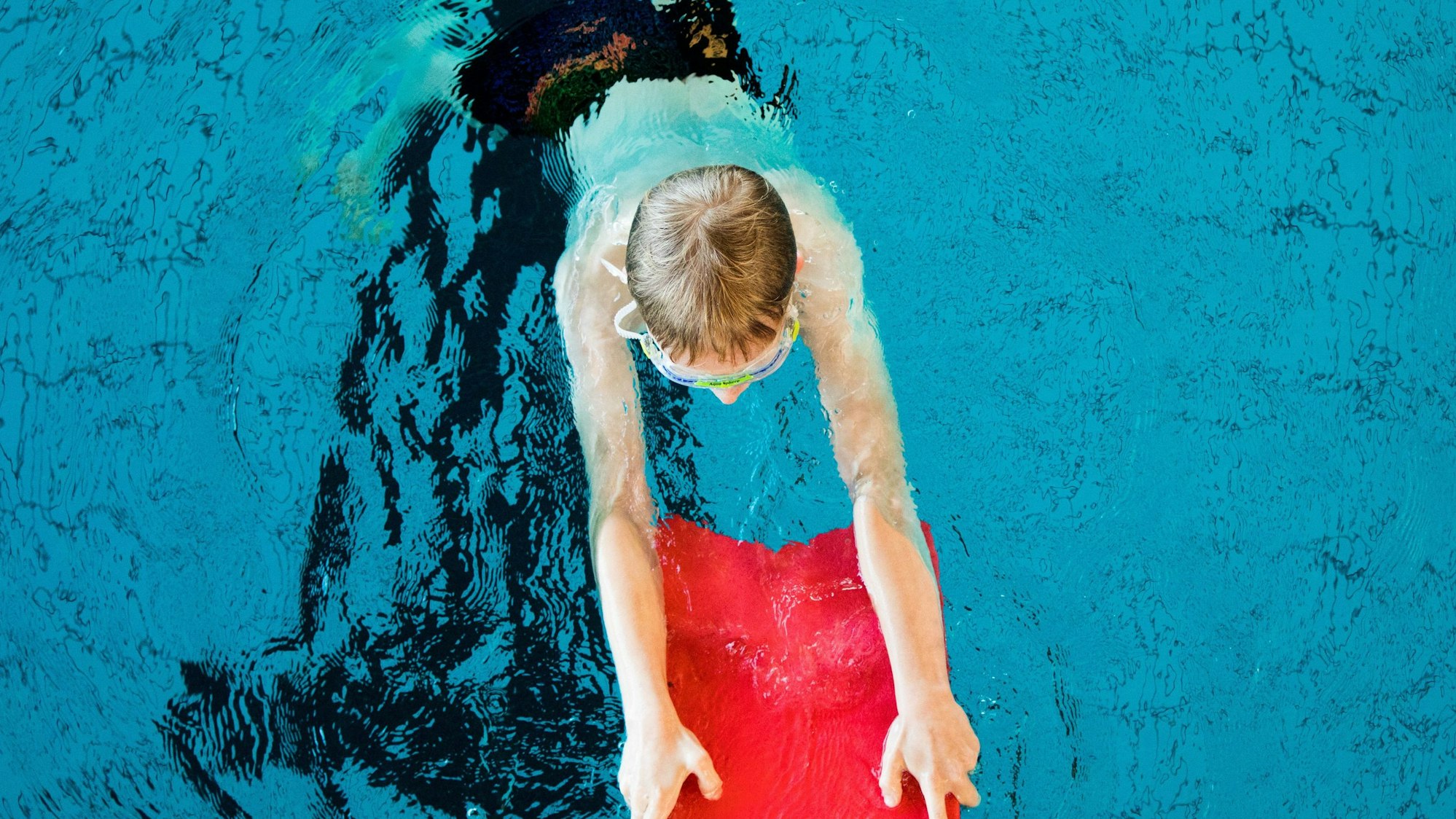 Ein Kind, von oben fotografiert, schwimmt mit einer Schwimmhilfe in einem Schwimmbecken.
