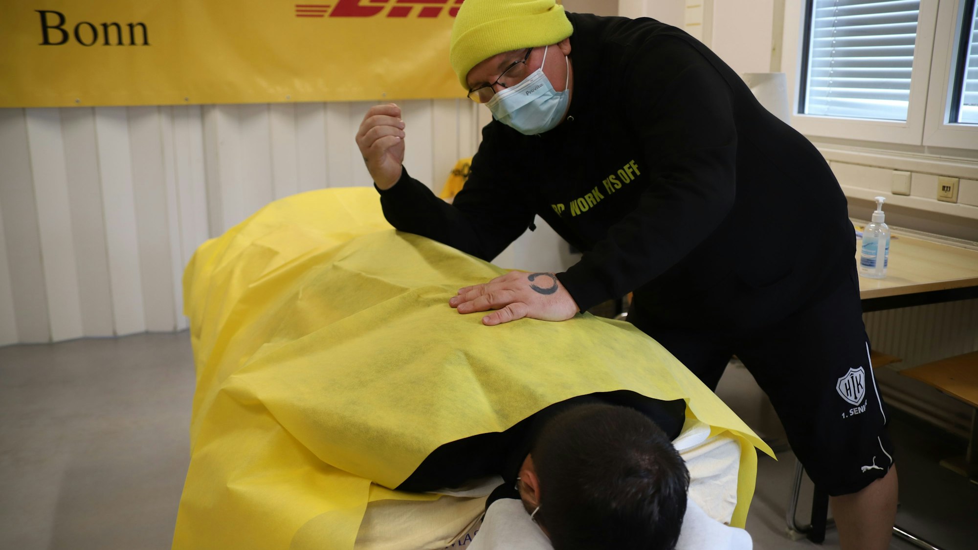 Christian Zwettler, der eine gelbe Mütze trägt, massiert einen seiner Kollegen, der auf einer Liege liegt.